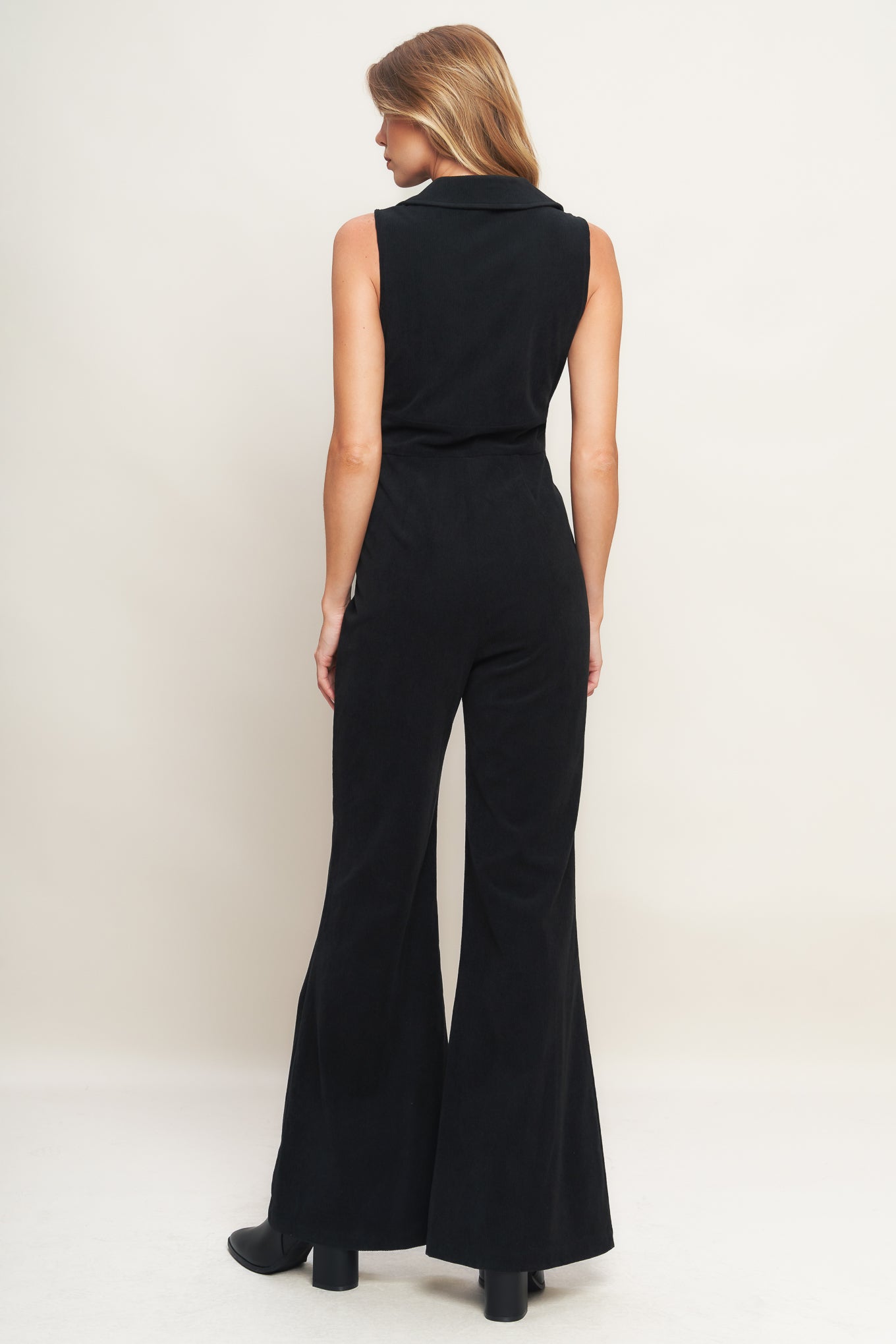 A solid corduroy jumpsuit featuring collar, V neckline, sleeveless, front zipper, waist yoke, side pocket and flare leg