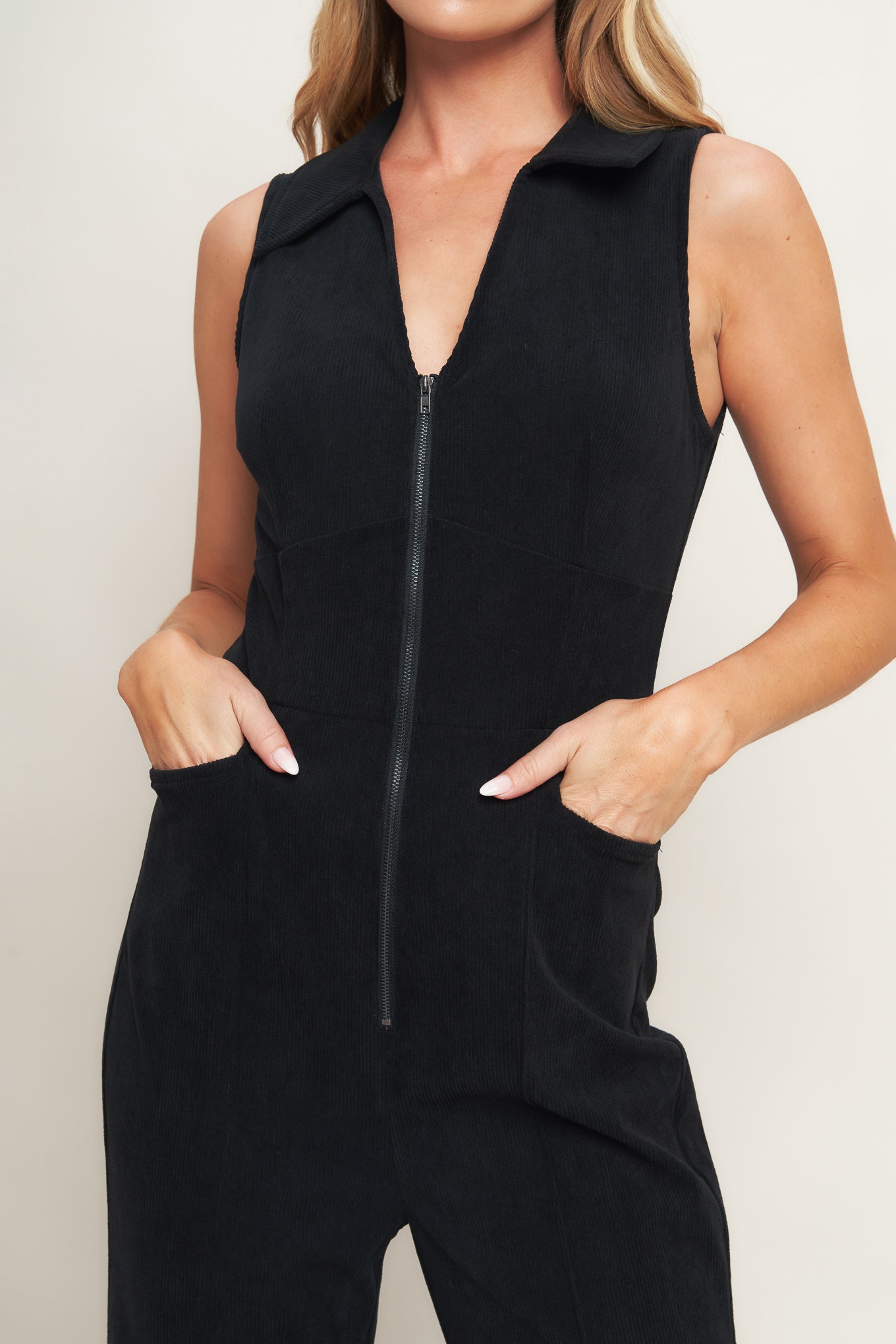 A solid corduroy jumpsuit featuring collar, V neckline, sleeveless, front zipper, waist yoke, side pocket and flare leg