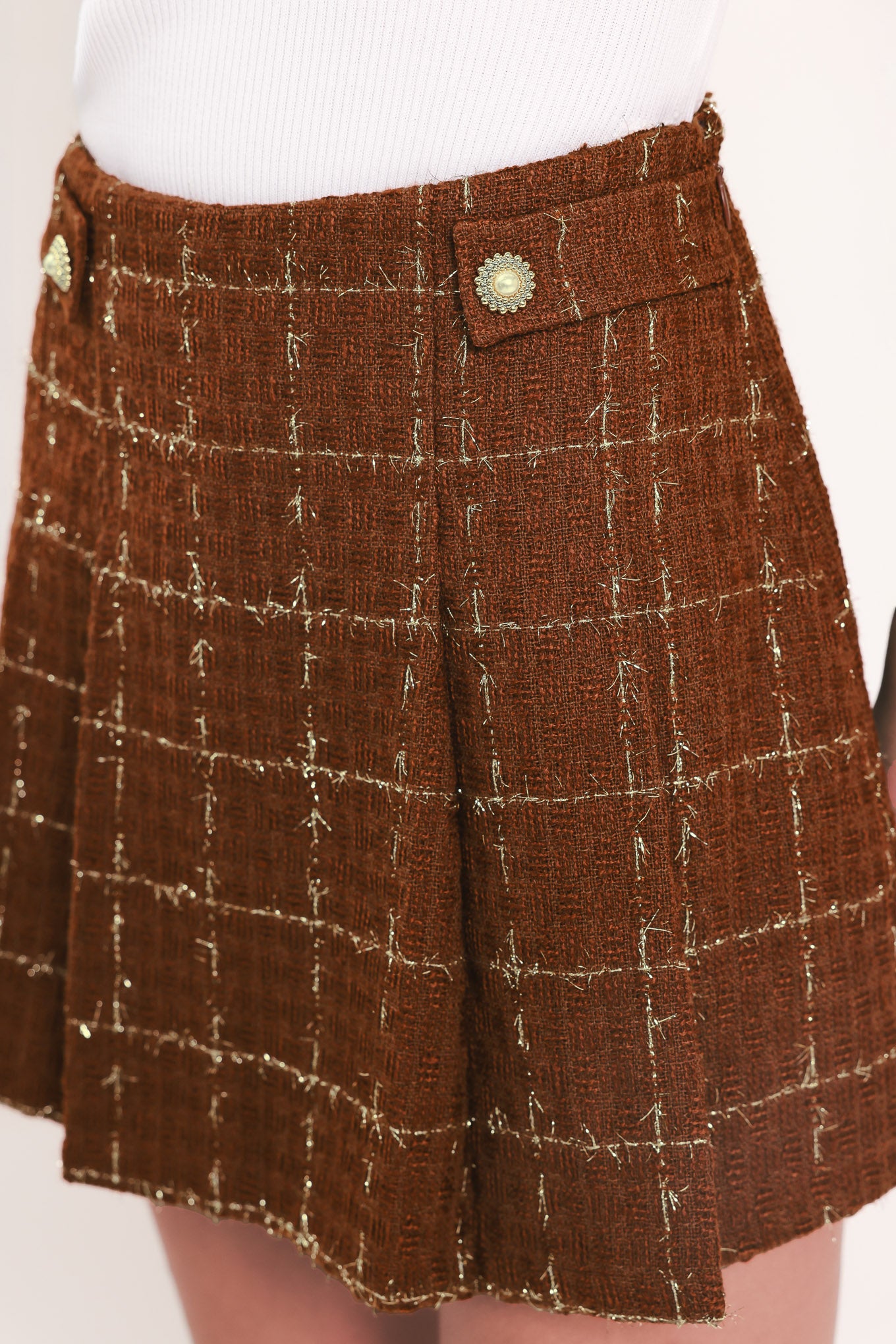A model wearing a brown/rust tweed mini skort with a white windowpane plaid pattern and gold-tone buttons | Flying Tomato