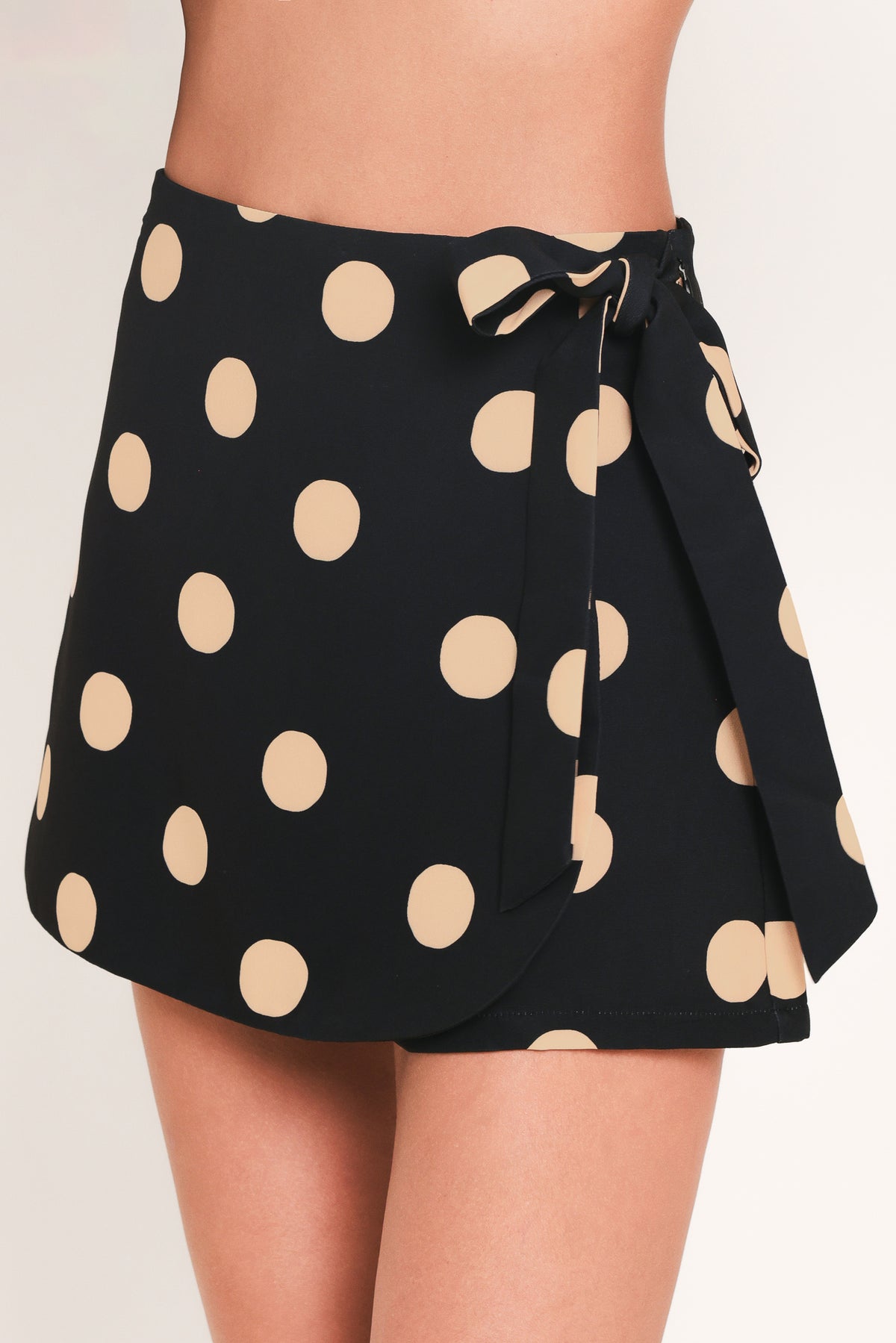 A woman wearing a black mini skort with large beige polka dots | Flying Tomato