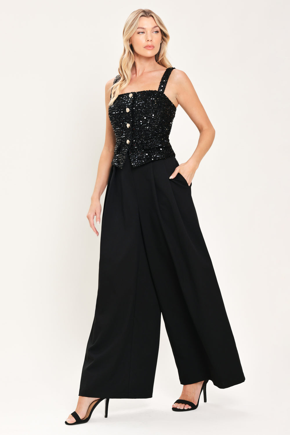Woman wearing a sleeveless, square-neckline black jumpsuit with sparkly top and solid bottoms | Flying Tomato