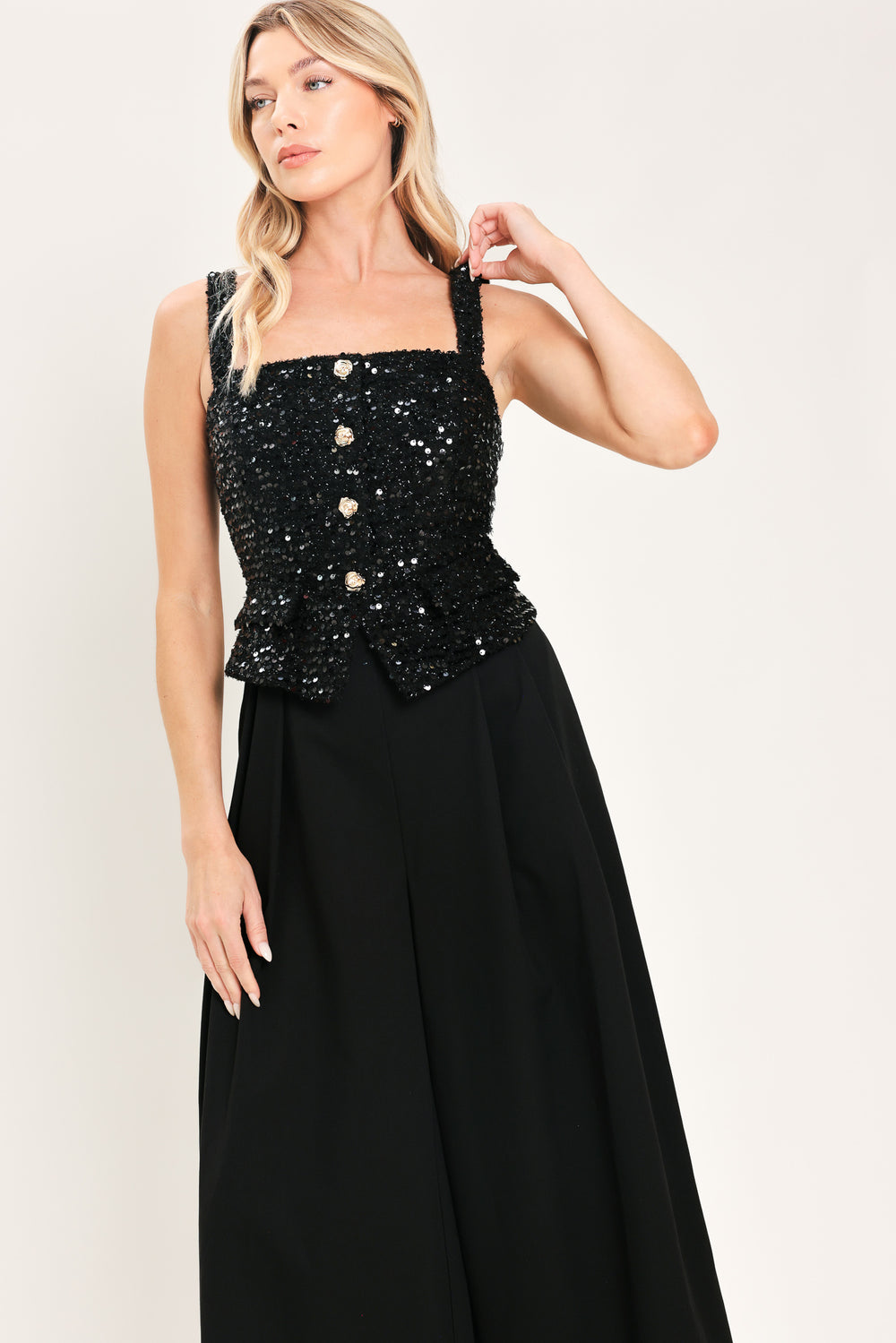 Woman wearing a sleeveless, square-neckline black jumpsuit with sparkly top and solid bottoms | Flying Tomato