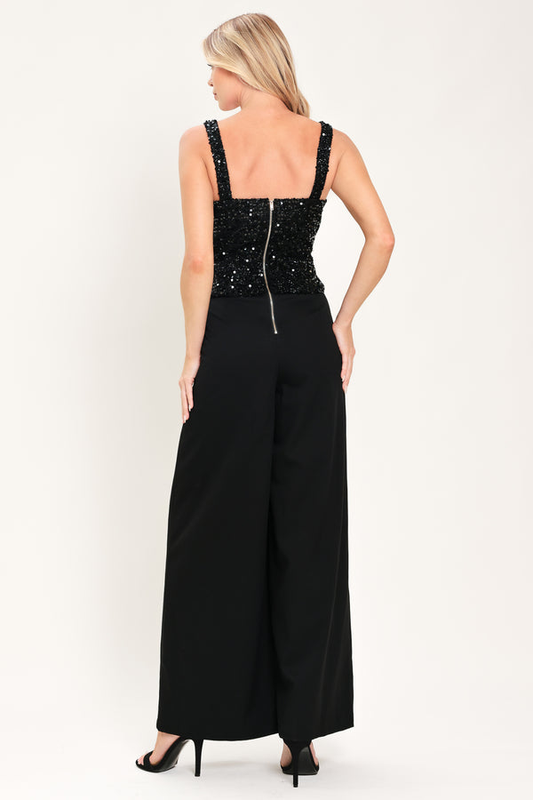 Woman wearing a sleeveless, square-neckline black jumpsuit with sparkly top and solid bottoms | Flying Tomato