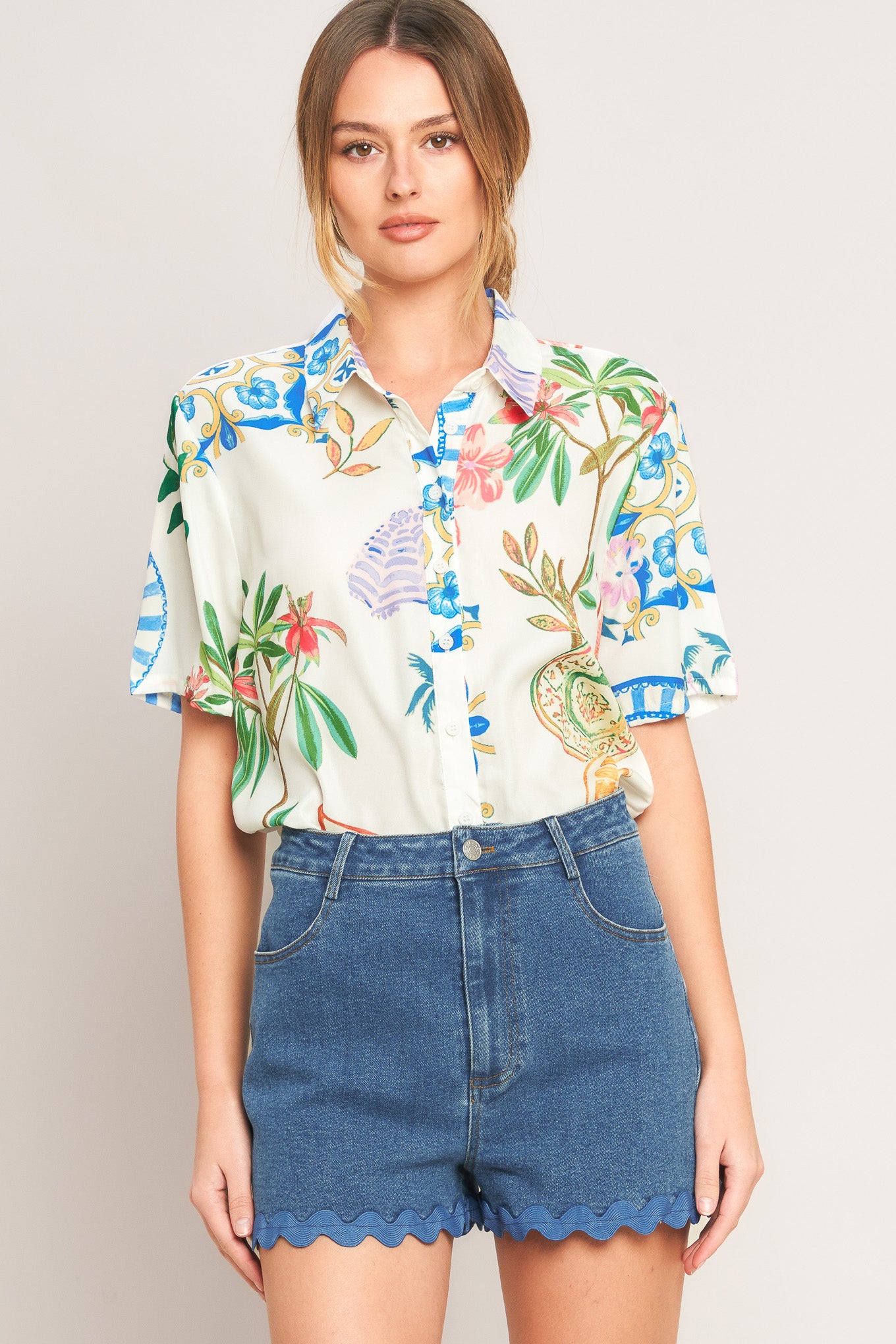 Woman wearing a colorful floral blouse and denim shorts on a plain background
