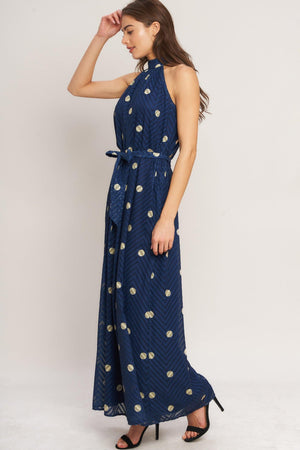A printed textured woven jumpsuit featuring halter neckline, self sash tie and back neck button closure