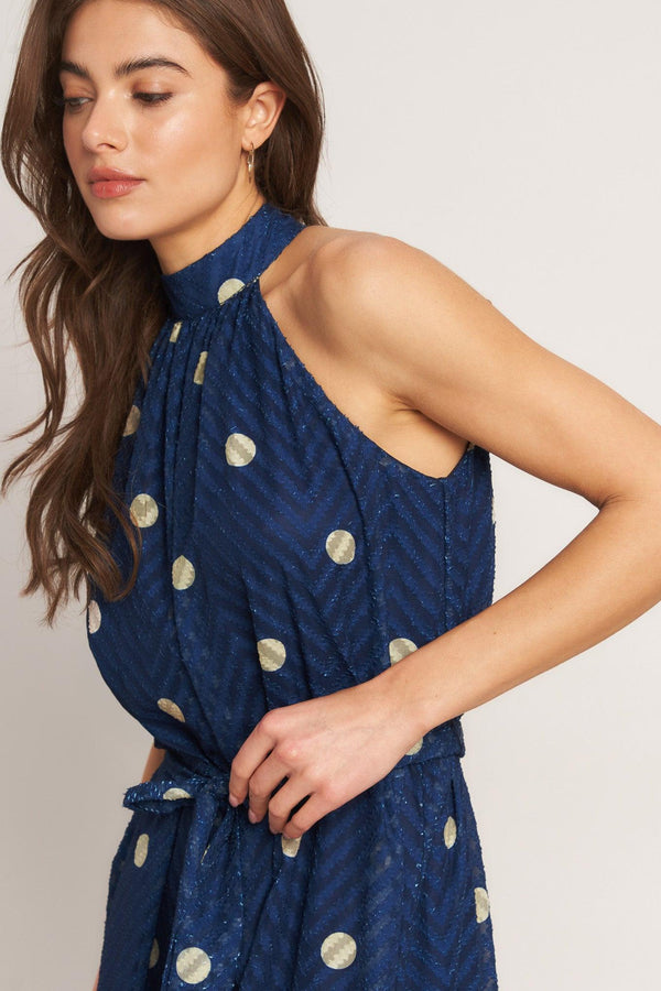 A printed textured woven jumpsuit featuring halter neckline, self sash tie and back neck button closure