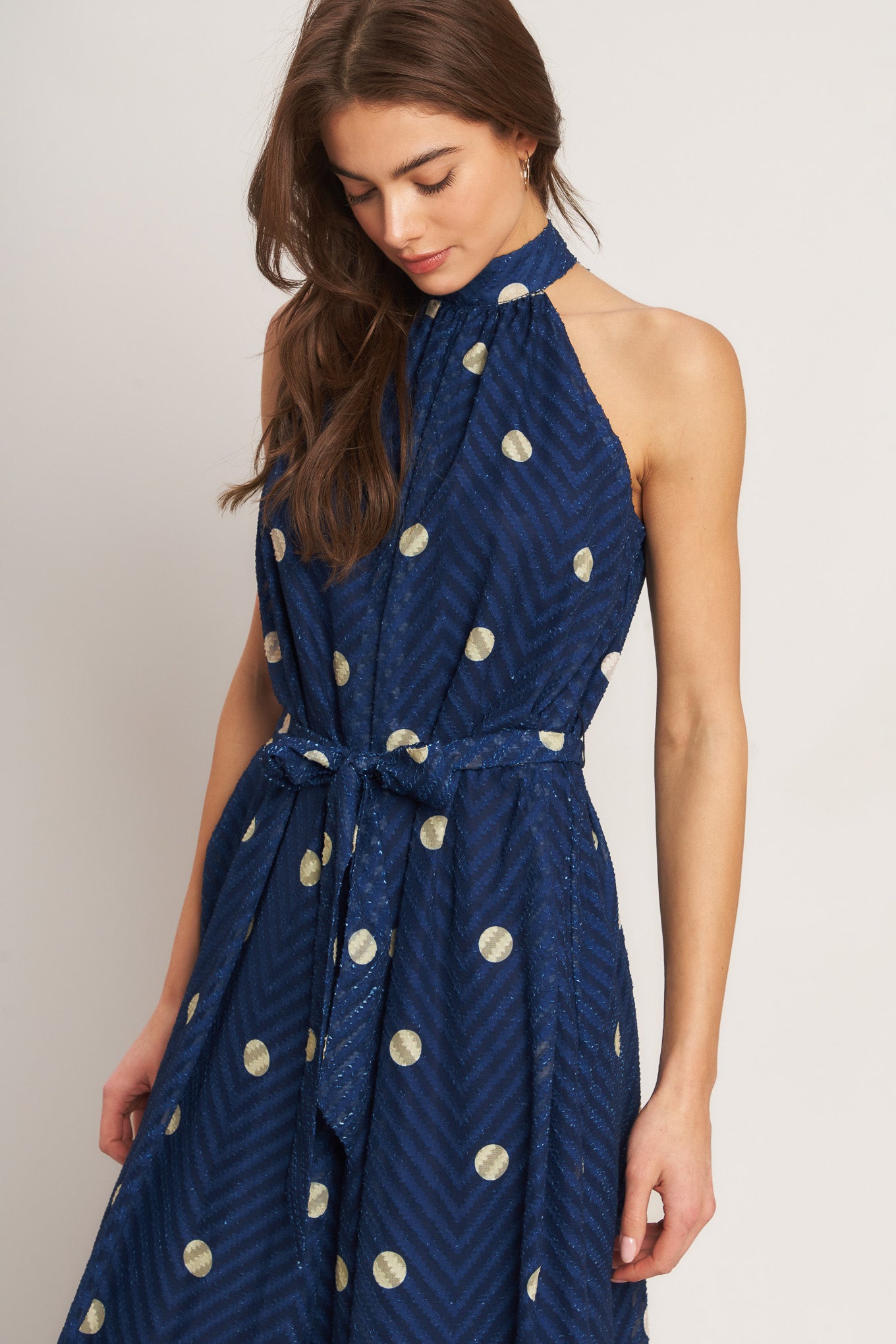 A printed textured woven jumpsuit featuring halter neckline, self sash tie and back neck button closure