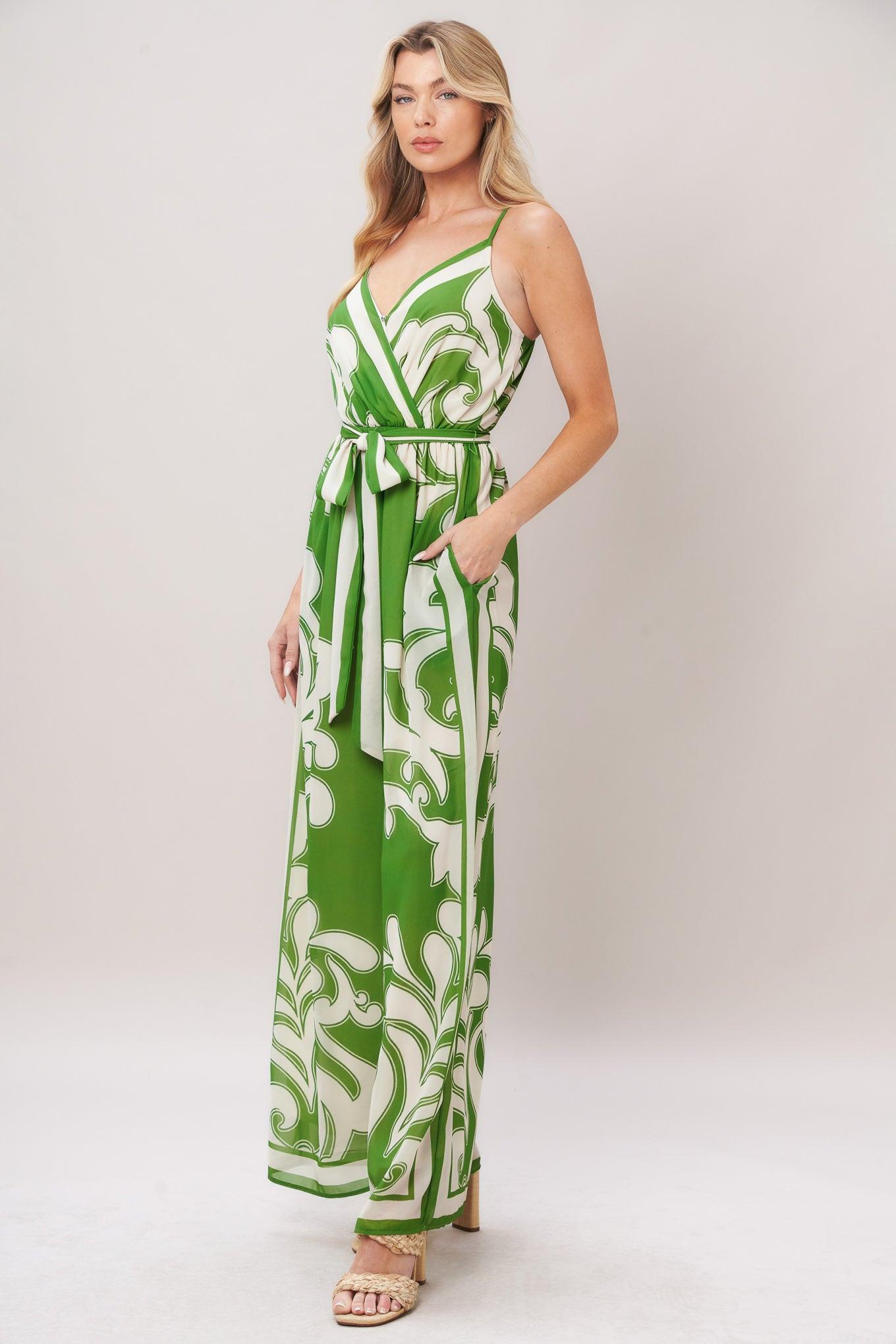 Woman wearing a green and white patterned printed woven jumpsuit featuring surplice neckline, straps, side pockets, self sash tie and wide leg