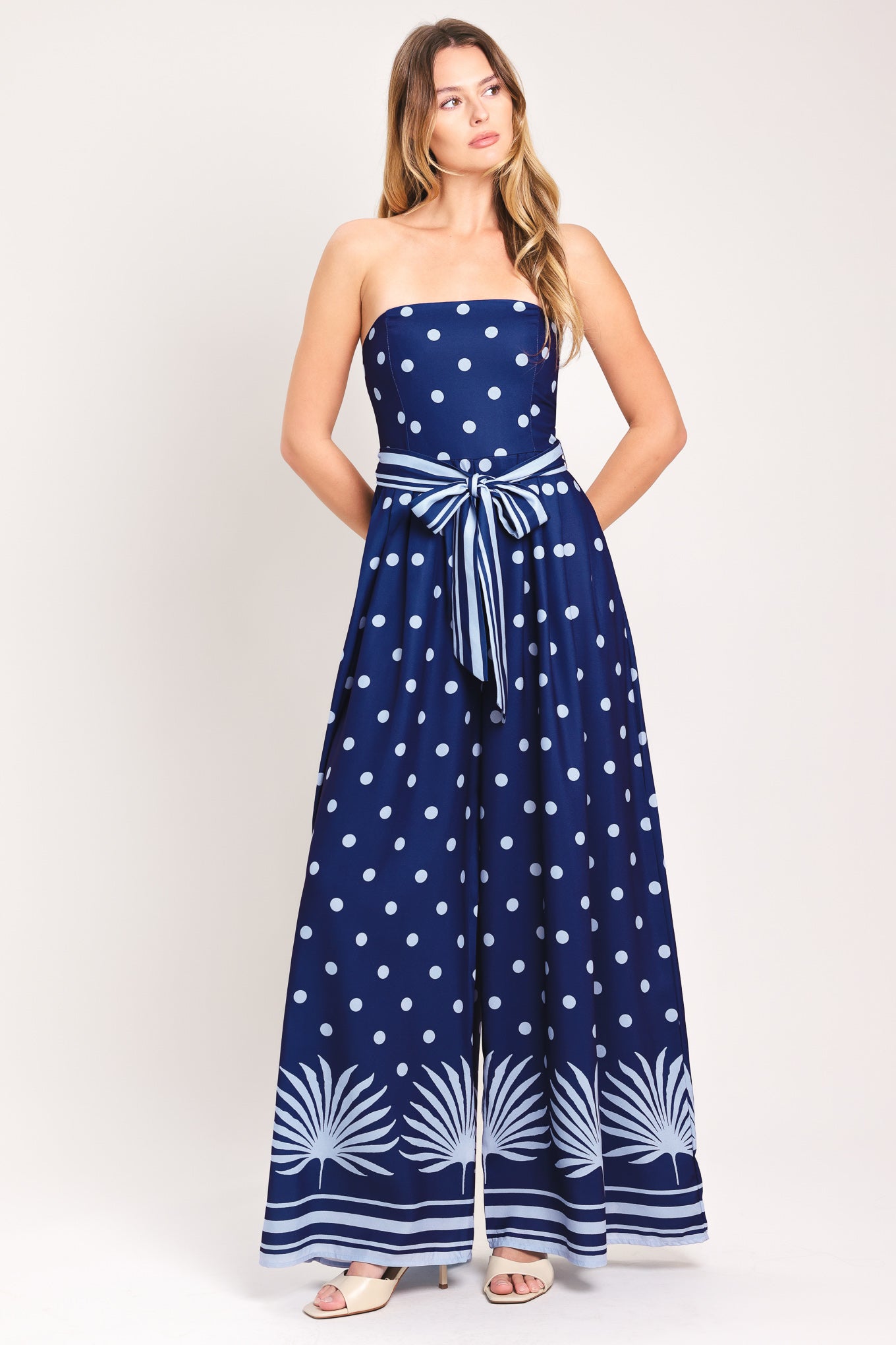Woman wearing a strapless navy blue jumpsuit with white polka dots and palm leaf patterns | Flying Tomato
