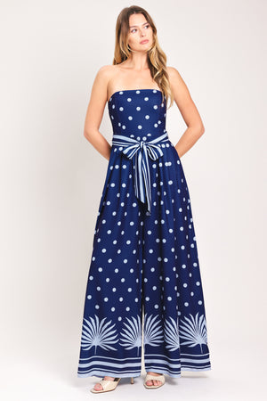 Woman wearing a strapless navy blue jumpsuit with white polka dots and palm leaf patterns | Flying Tomato