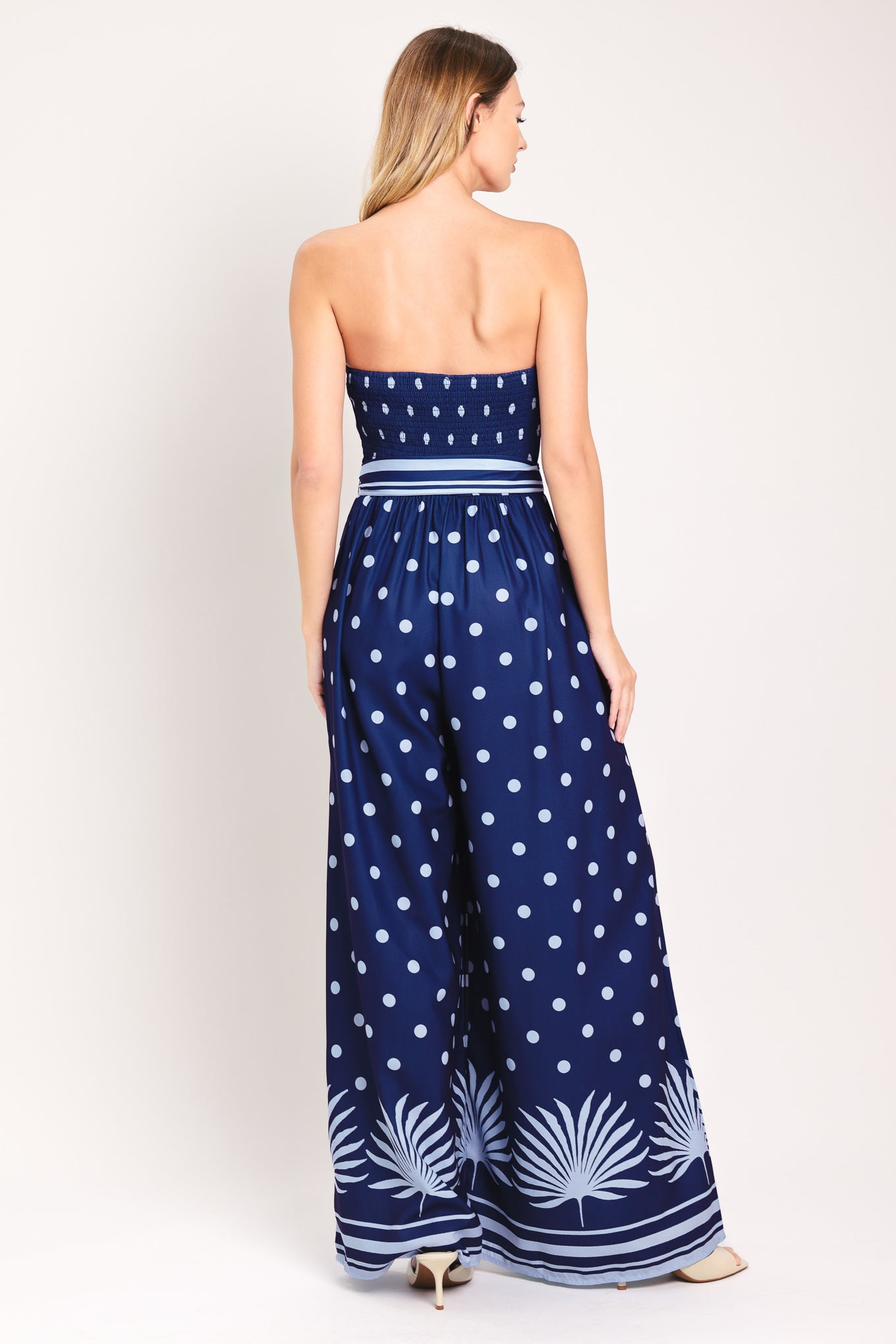 Woman wearing a strapless navy blue jumpsuit with white polka dots and palm leaf patterns | Flying Tomato