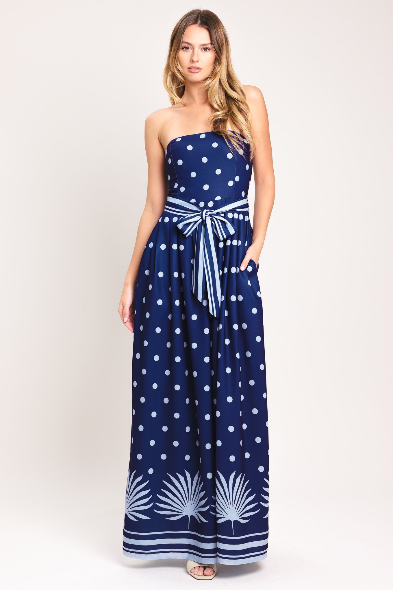 Woman wearing a strapless navy blue jumpsuit with white polka dots and palm leaf patterns | Flying Tomato