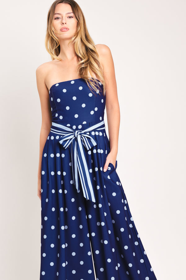 Woman wearing a strapless navy blue jumpsuit with white polka dots and palm leaf patterns | Flying Tomato