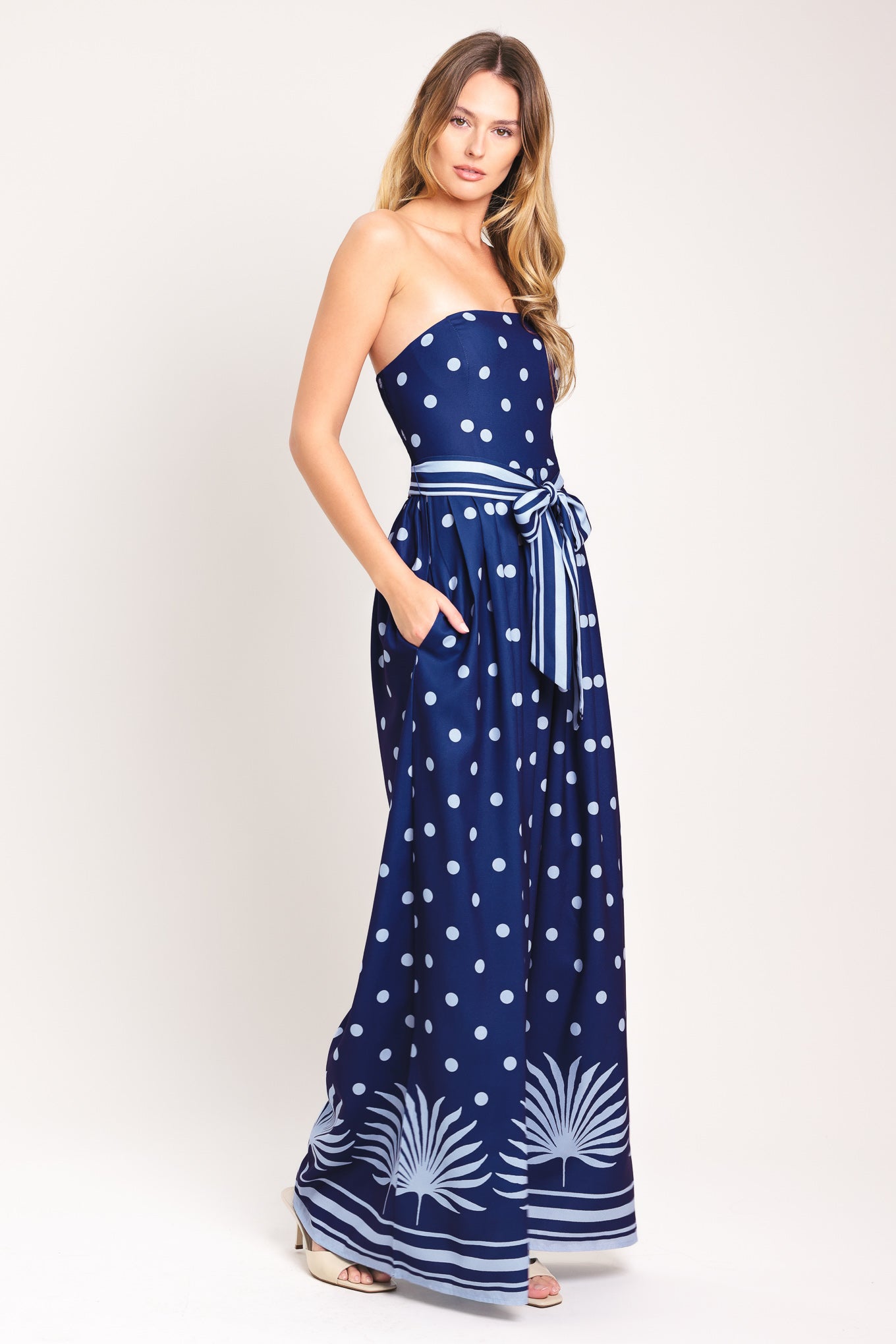 Woman wearing a strapless navy blue jumpsuit with white polka dots and palm leaf patterns | Flying Tomato