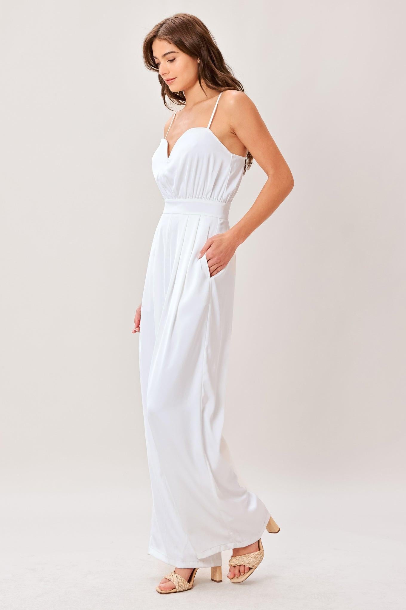 A solid woven jumpsuit featuring sweetheart neckline, straps, side pockets, wide leg and back zipper closure