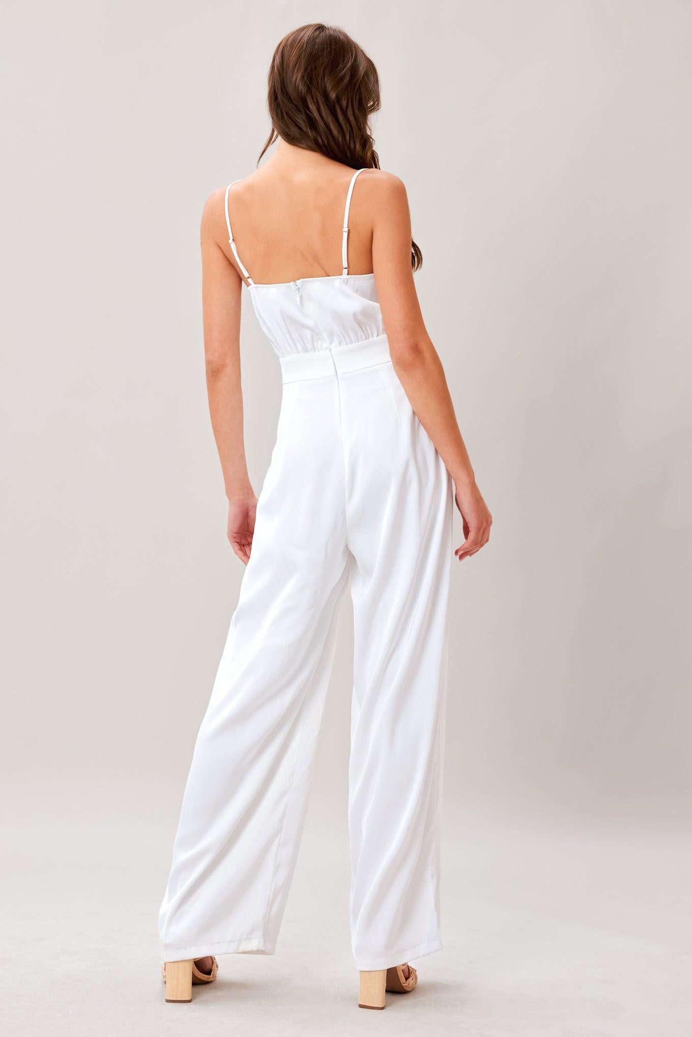 A solid woven jumpsuit featuring sweetheart neckline, straps, side pockets, wide leg and back zipper closure