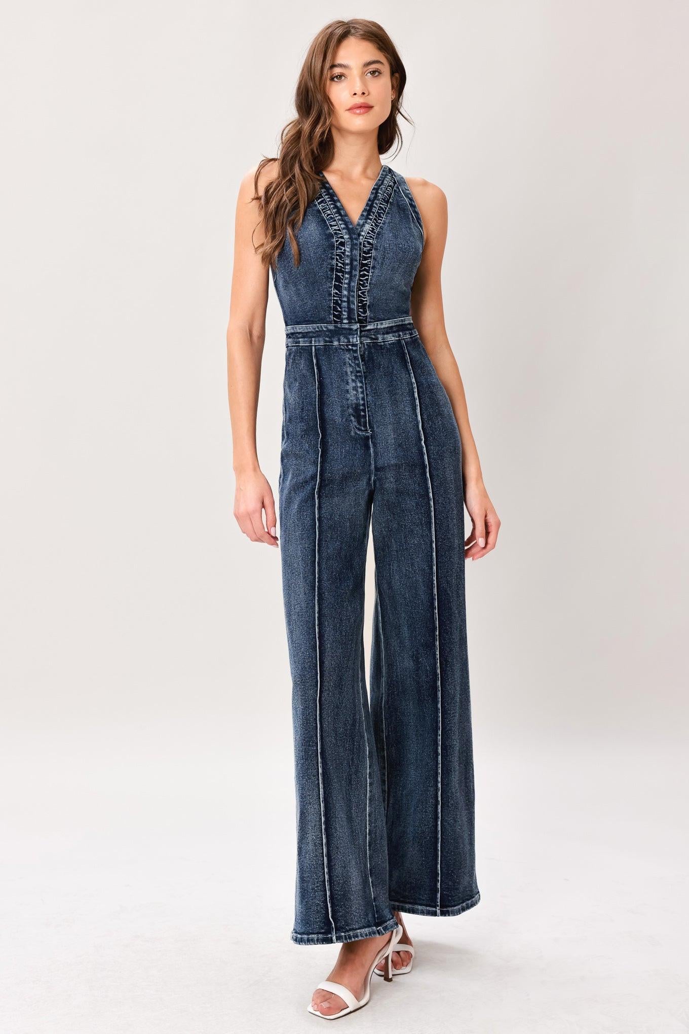 Woman wearing a washed denim jumpsuit featuring V neckline, front closure, center leg seam and straight leg