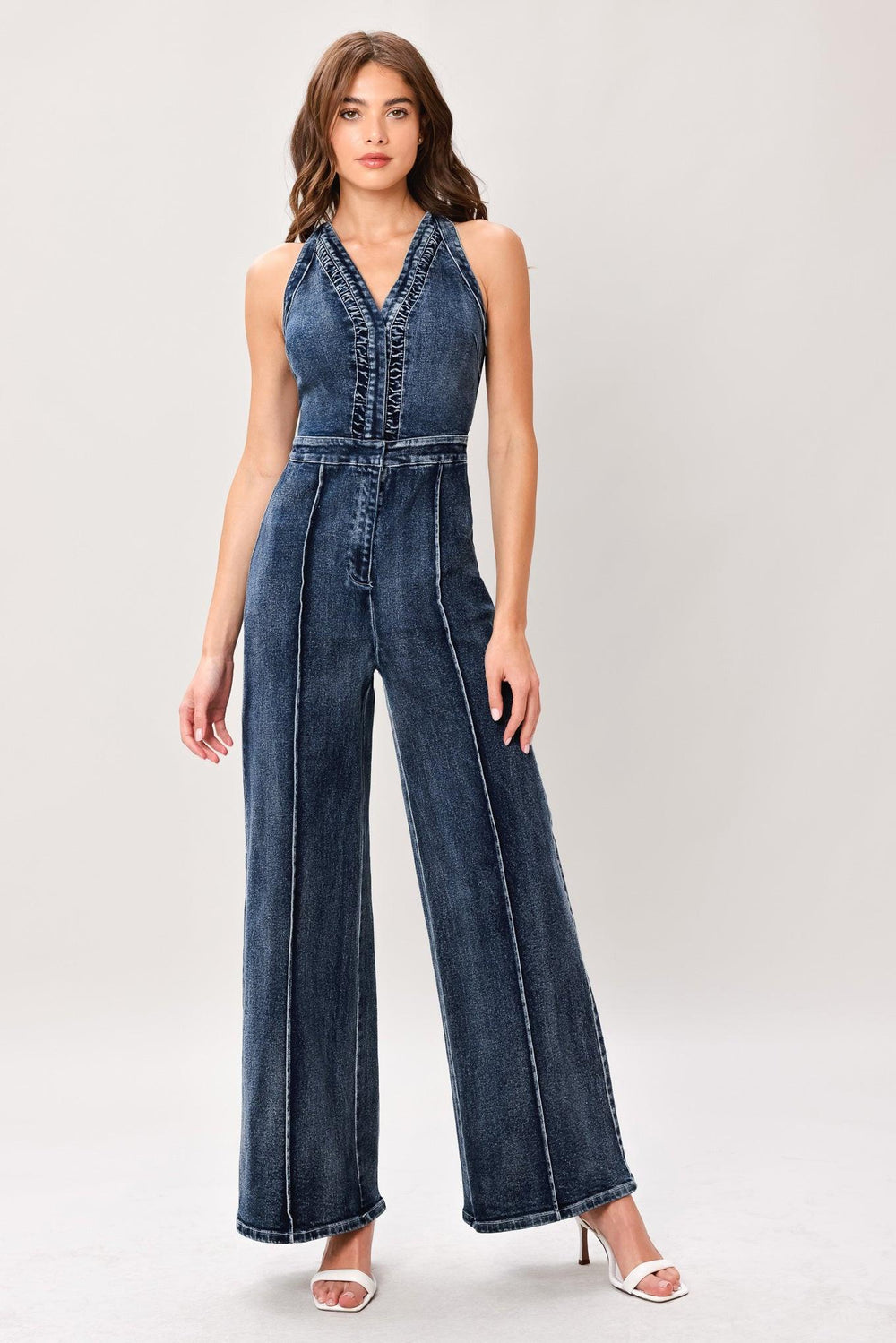 Woman wearing a washed denim jumpsuit featuring V neckline, front closure, center leg seam and straight leg