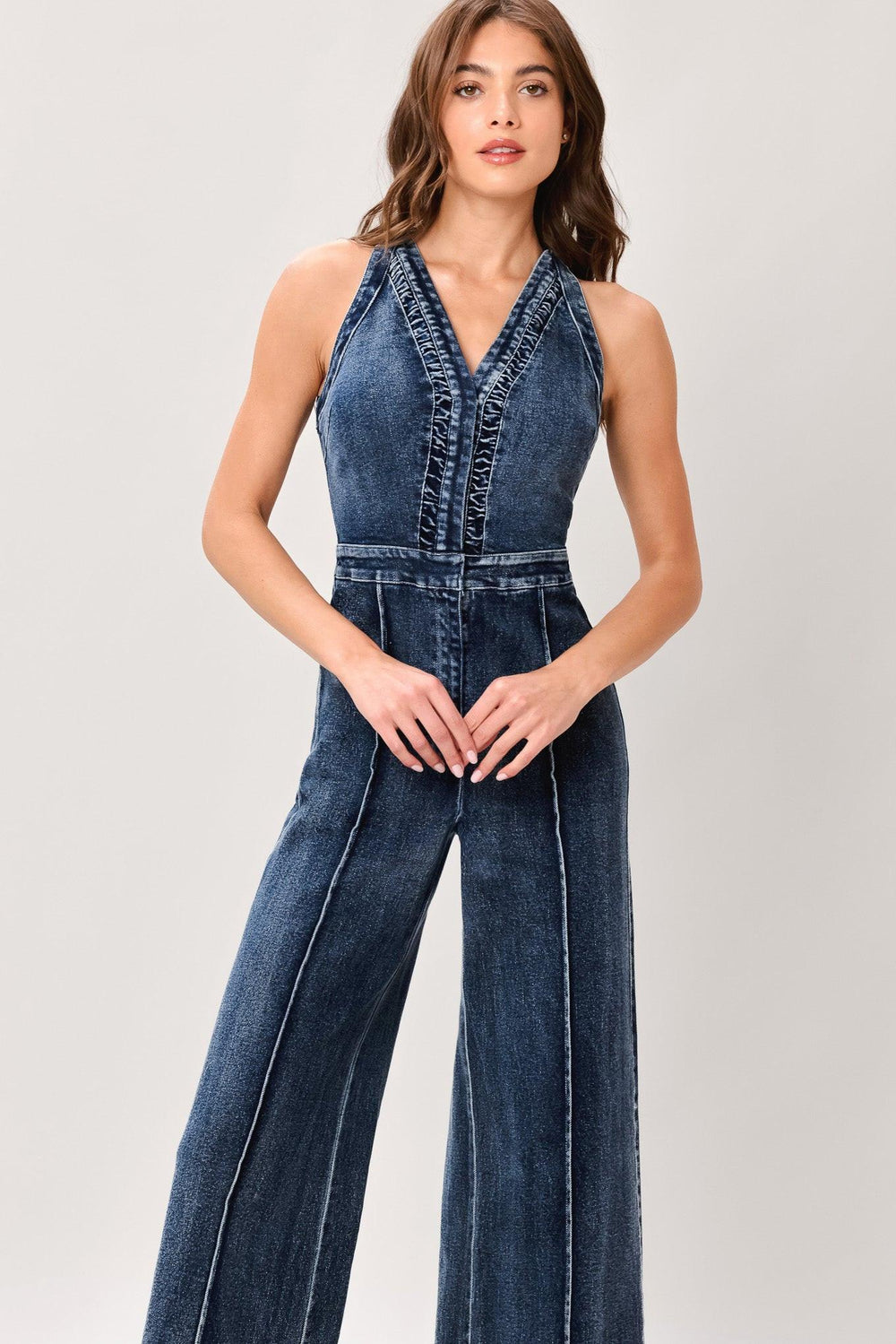 Woman wearing a washed denim jumpsuit featuring V neckline, front closure, center leg seam and straight leg