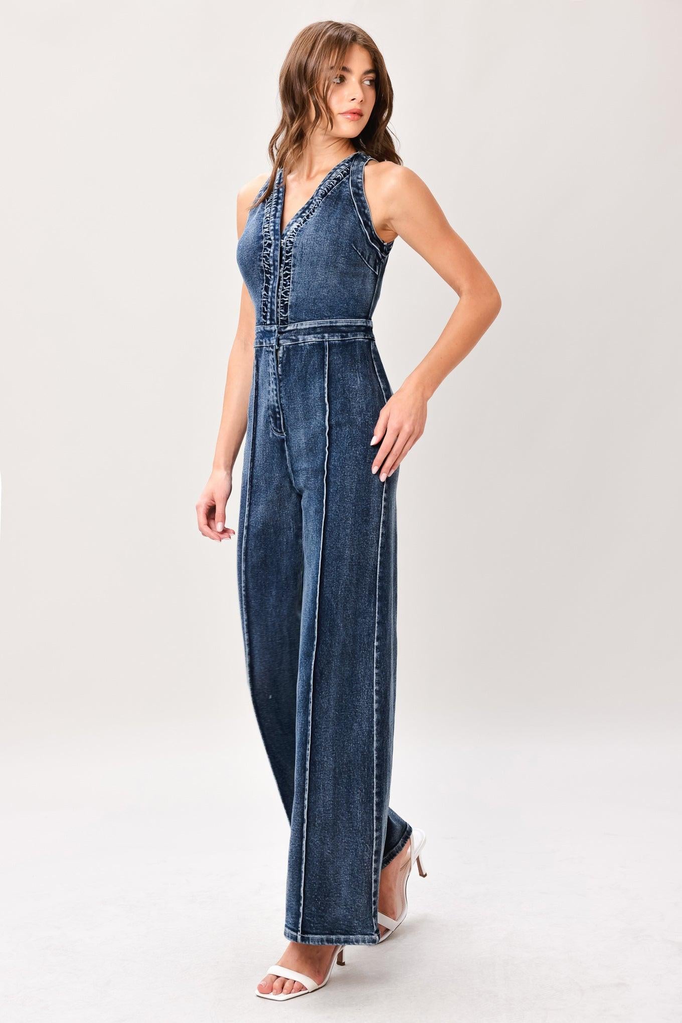 Woman wearing a washed denim jumpsuit featuring V neckline, front closure, center leg seam and straight leg