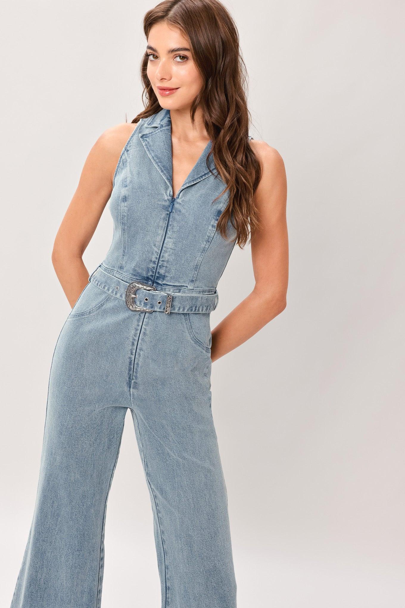 Woman wearing a washed denim jumpsuit featuring collar, sleeveless, front zipper, self belt and flare leg