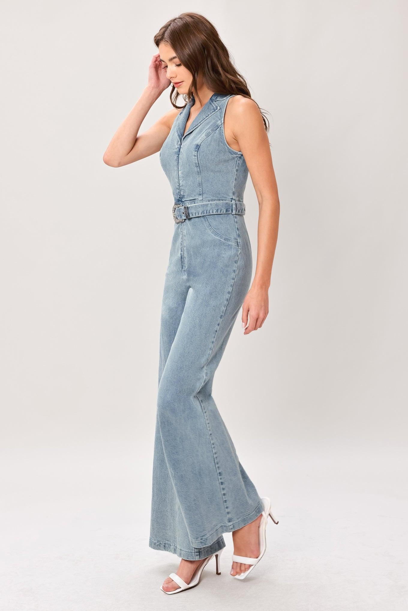 Woman wearing a washed denim jumpsuit featuring collar, sleeveless, front zipper, self belt and flare leg