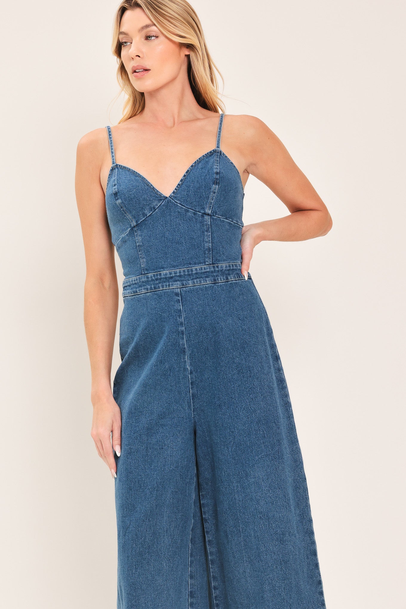 Woman wearing a blue denim jumpsuit featuring cami, top straps, wide leg and back zipper closure | Flying Tomato