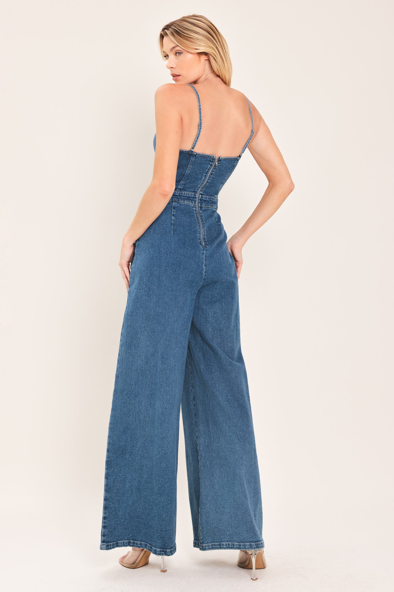 Woman wearing a blue denim jumpsuit featuring cami, top straps, wide leg and back zipper closure | Flying Tomato