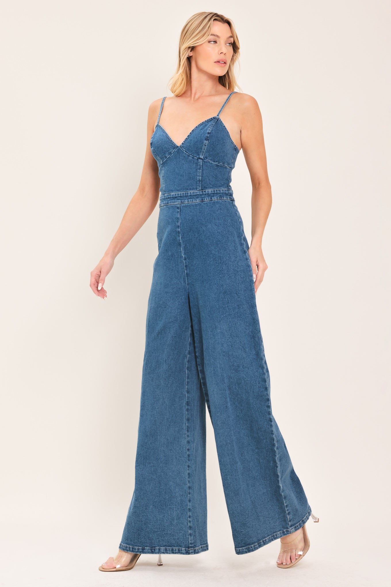 Woman wearing a blue denim jumpsuit featuring cami, top straps, wide leg and back zipper closure | Flying Tomato