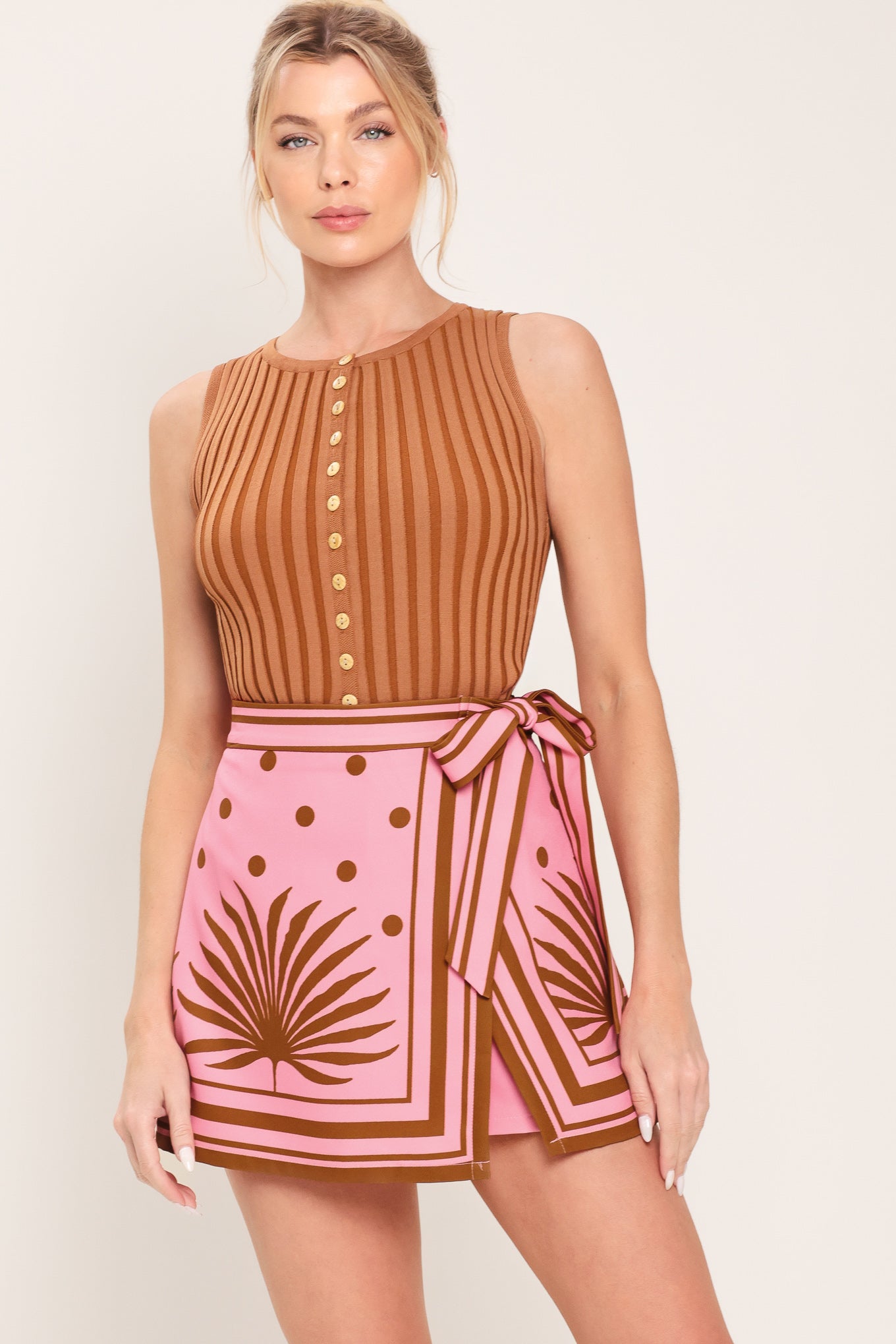 Woman wearing a pink skort with brown polka dots and printed palms featuring a side bow tie and zipper closure | Flying Tomato