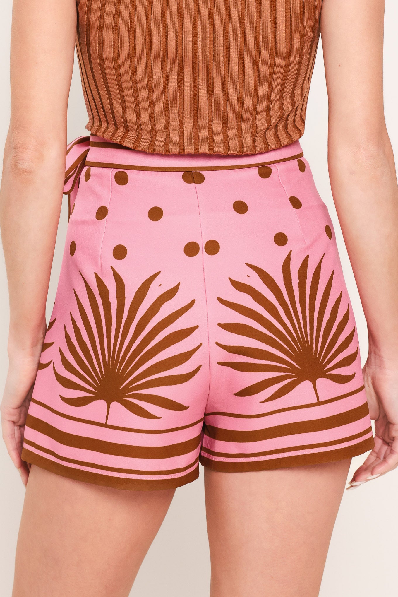 Woman wearing a pink skort with brown polka dots and printed palms featuring a side bow tie and zipper closure | Flying Tomato
