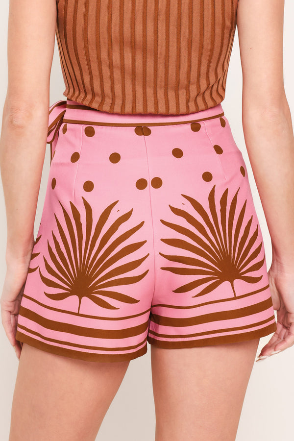 Woman wearing a pink skort with brown polka dots and printed palms featuring a side bow tie and zipper closure | Flying Tomato