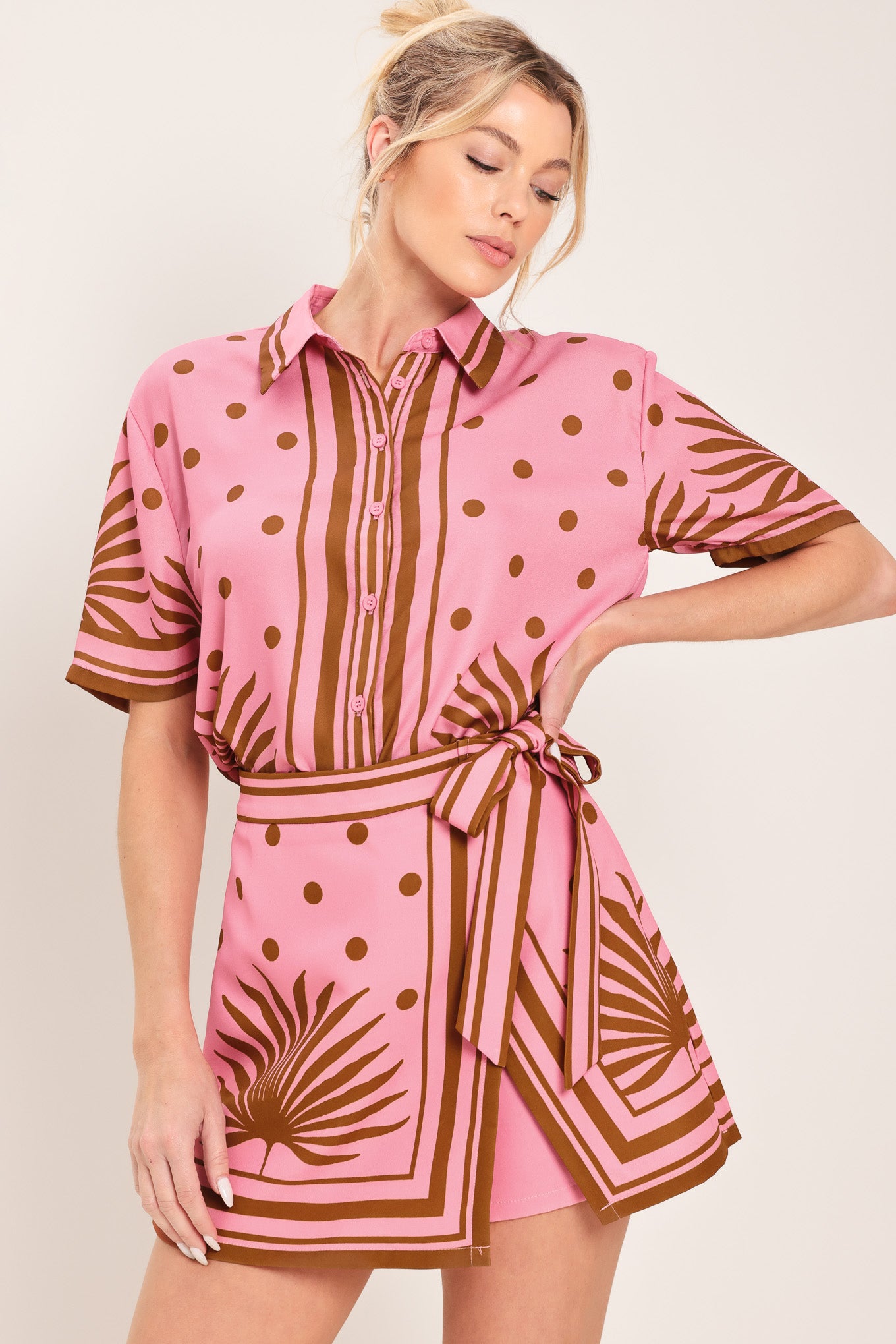 Woman wearing a pink skort with brown polka dots and printed palms featuring a side bow tie and zipper closure | Flying Tomato