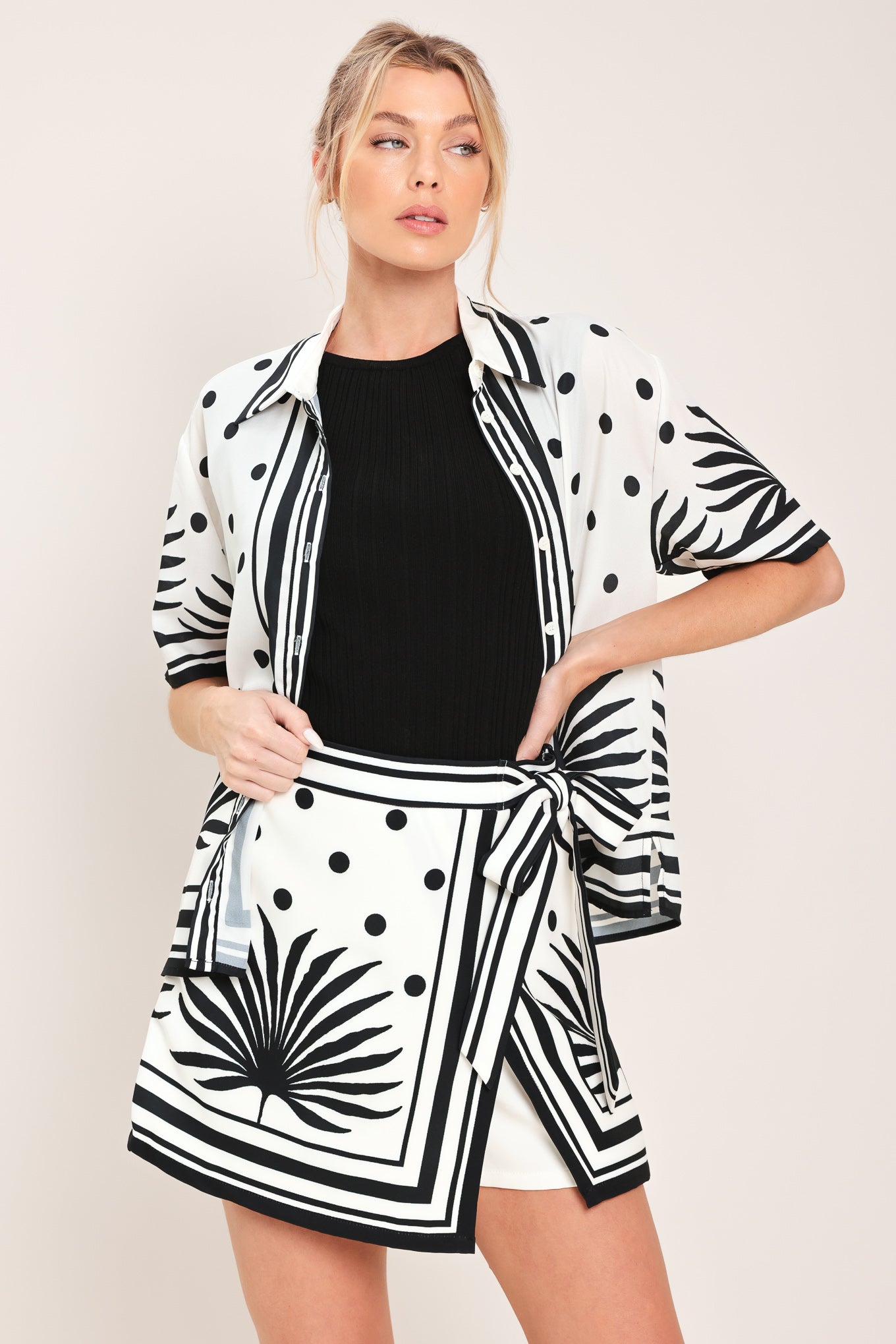 Woman wearing a white skort with black polka dots and printed palms featuring a side bow tie and zipper closure | Flying Tomato
