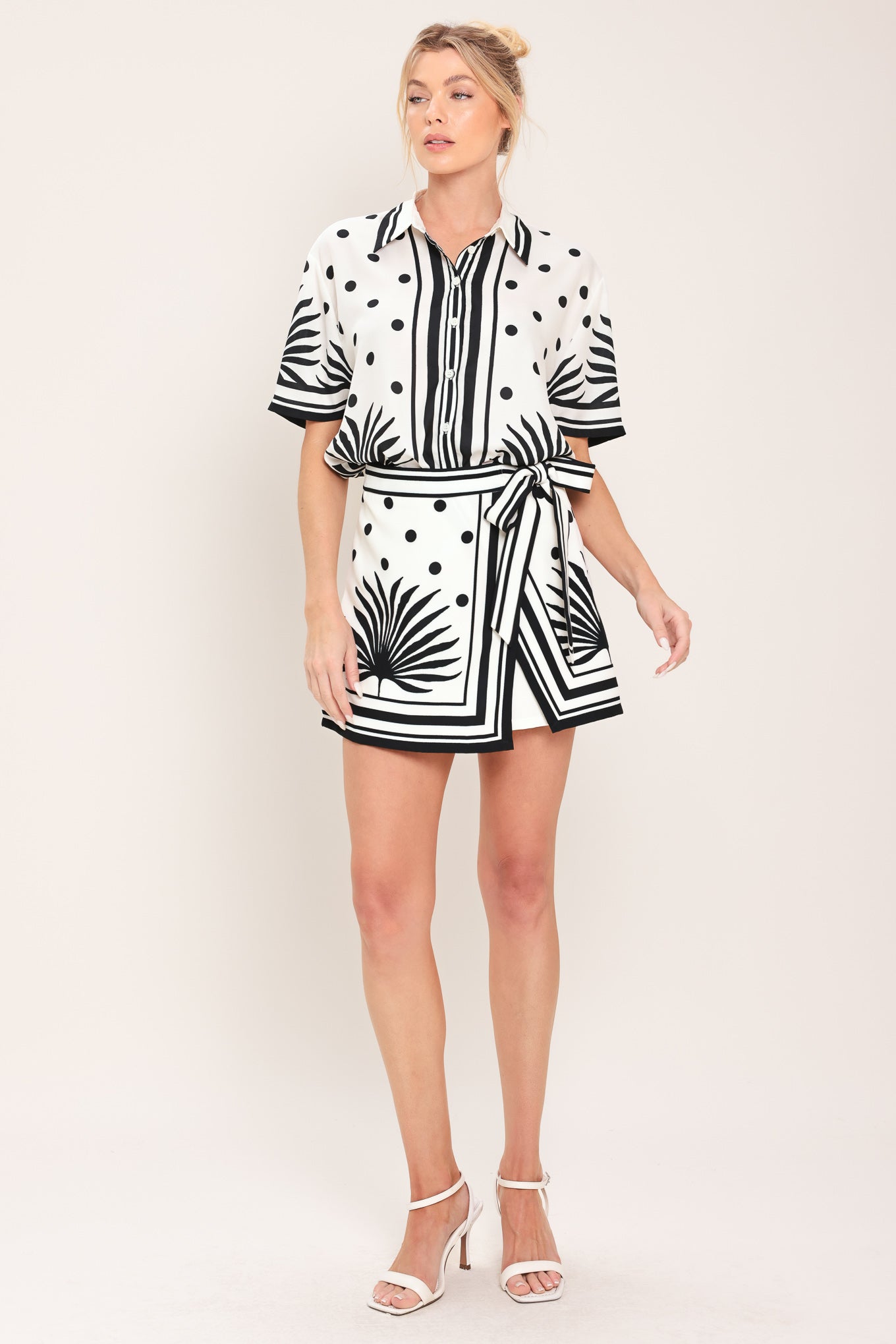 Woman wearing a white skort with black polka dots and printed palms featuring a side bow tie and zipper closure | Flying Tomato