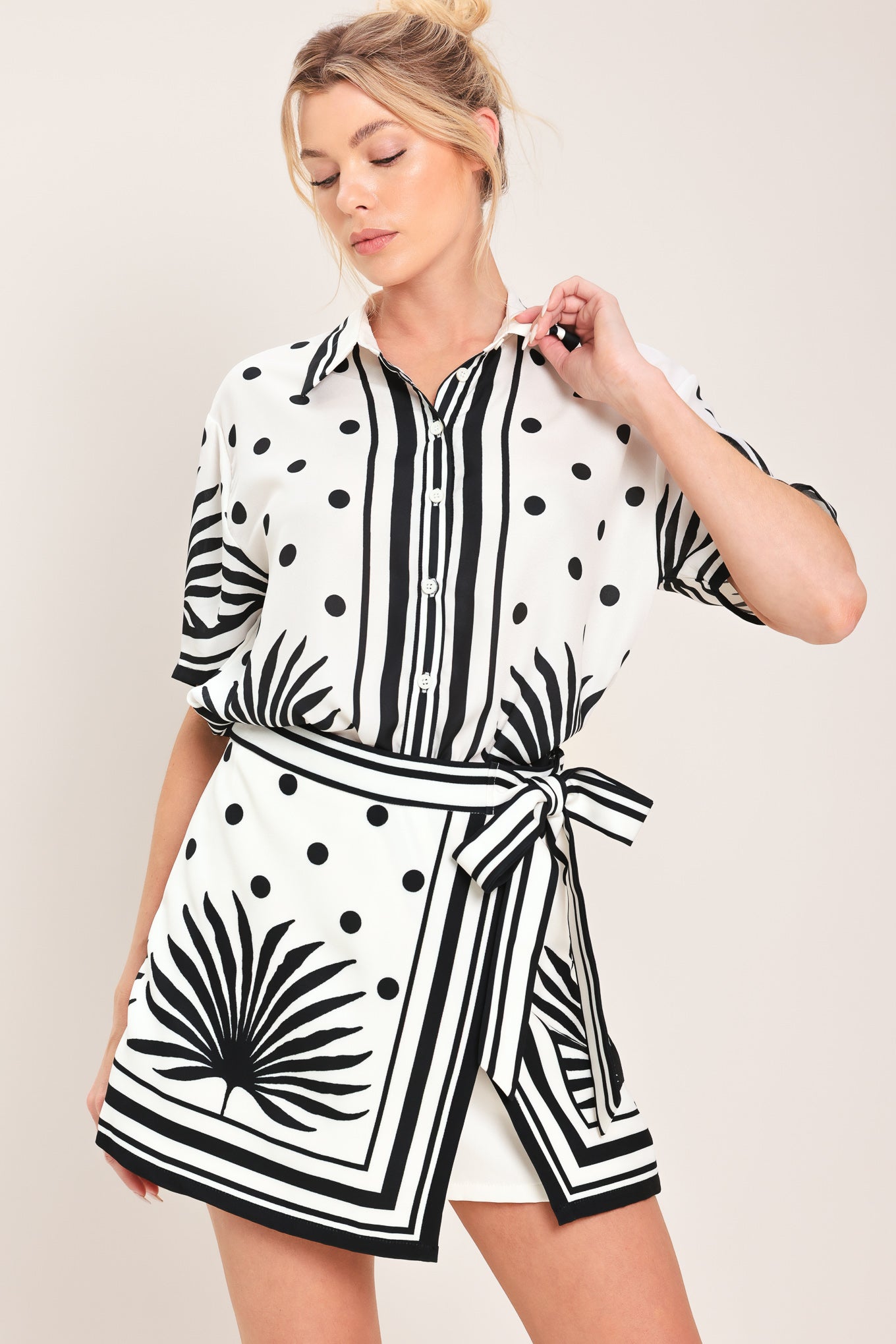 Woman wearing a white skort with black polka dots and printed palms featuring a side bow tie and zipper closure | Flying Tomato