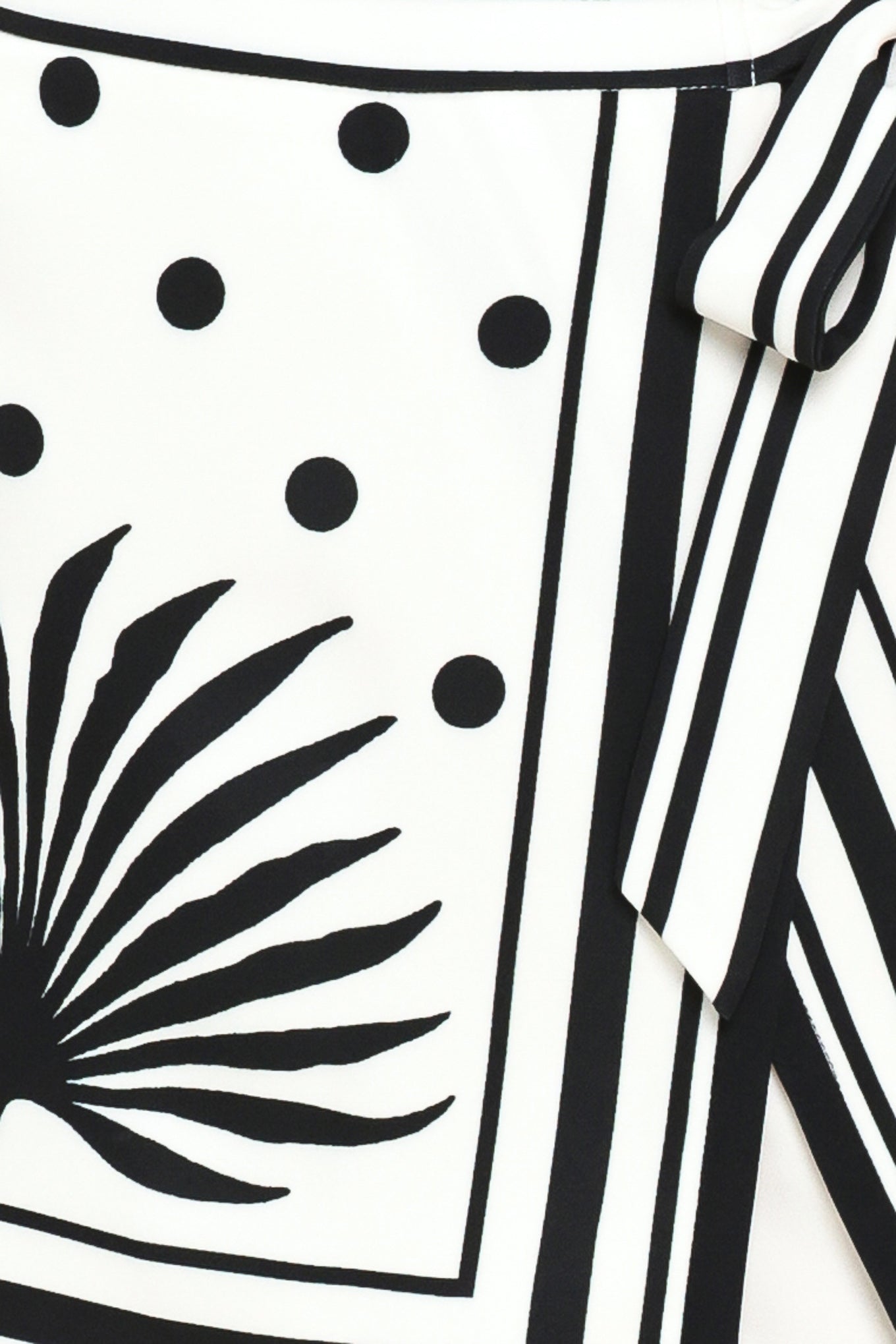 Close up of a white skort with black polka dots and printed palms featuring a side bow tie and zipper closure | Flying Tomato