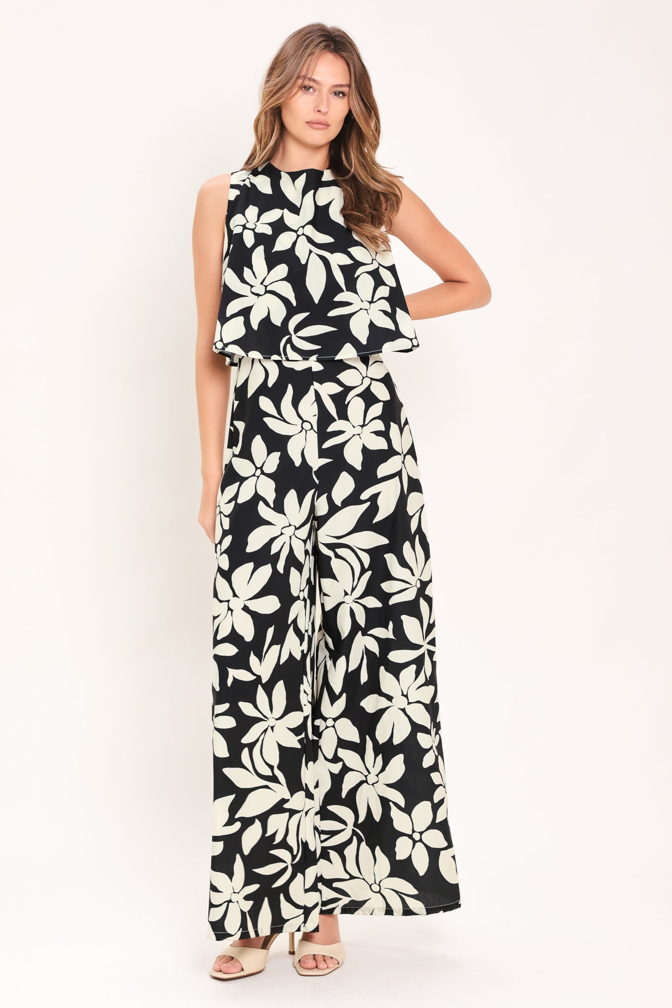 Woman wearing a black and white floral wide leg jumpsuit featuring round neckline, popover, split back with zipper closure | Flying Tomato