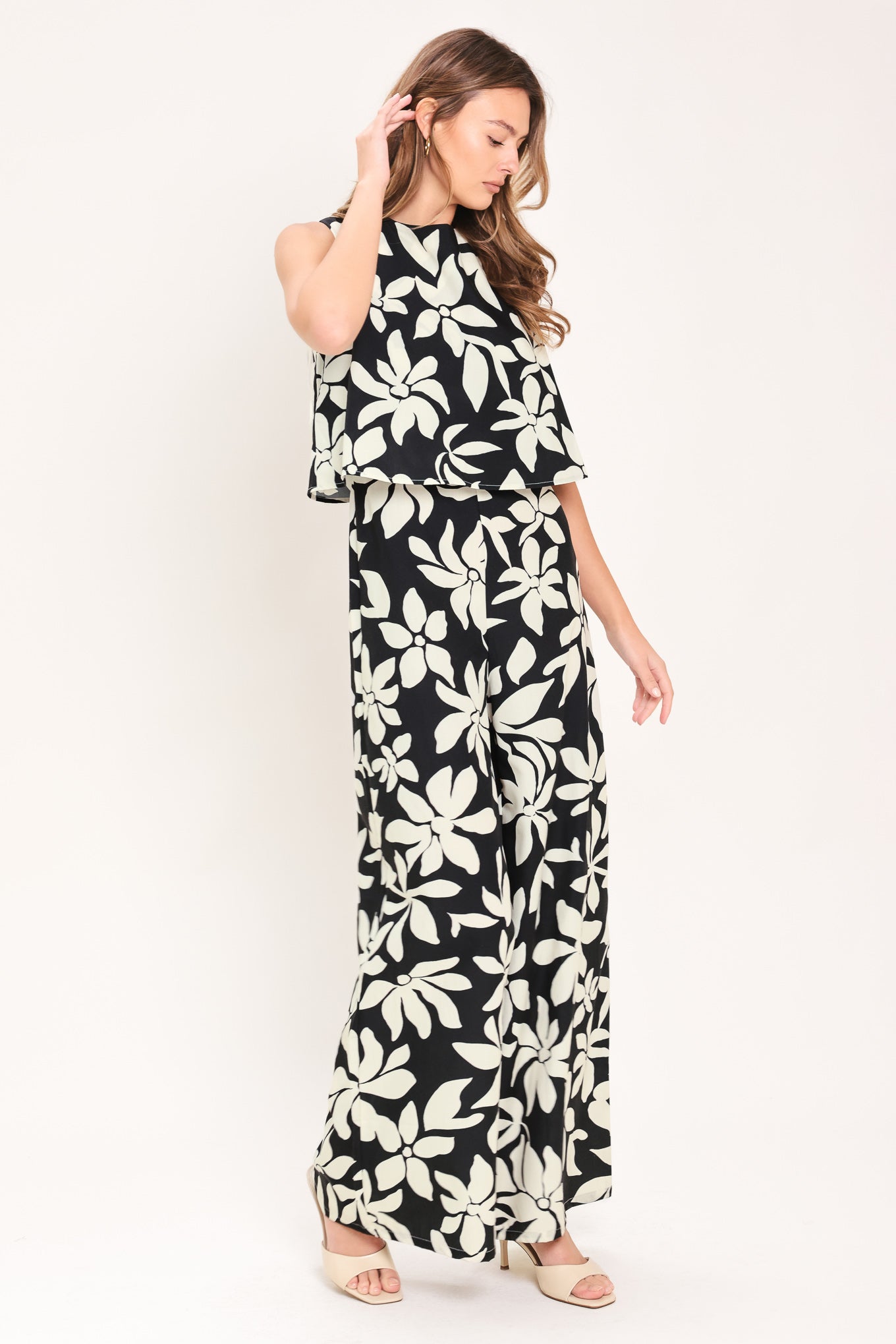 Woman wearing a black and white floral wide leg jumpsuit featuring round neckline, popover, split back with zipper closure | Flying Tomato