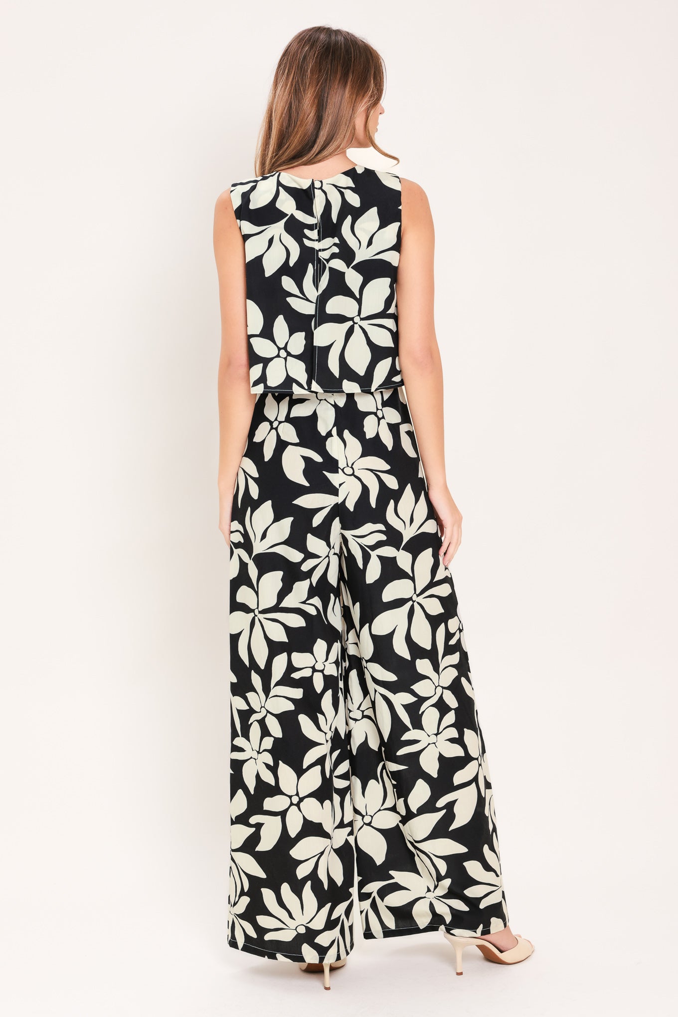 Woman wearing a black and white floral wide leg jumpsuit featuring round neckline, popover, split back with zipper closure | Flying Tomato