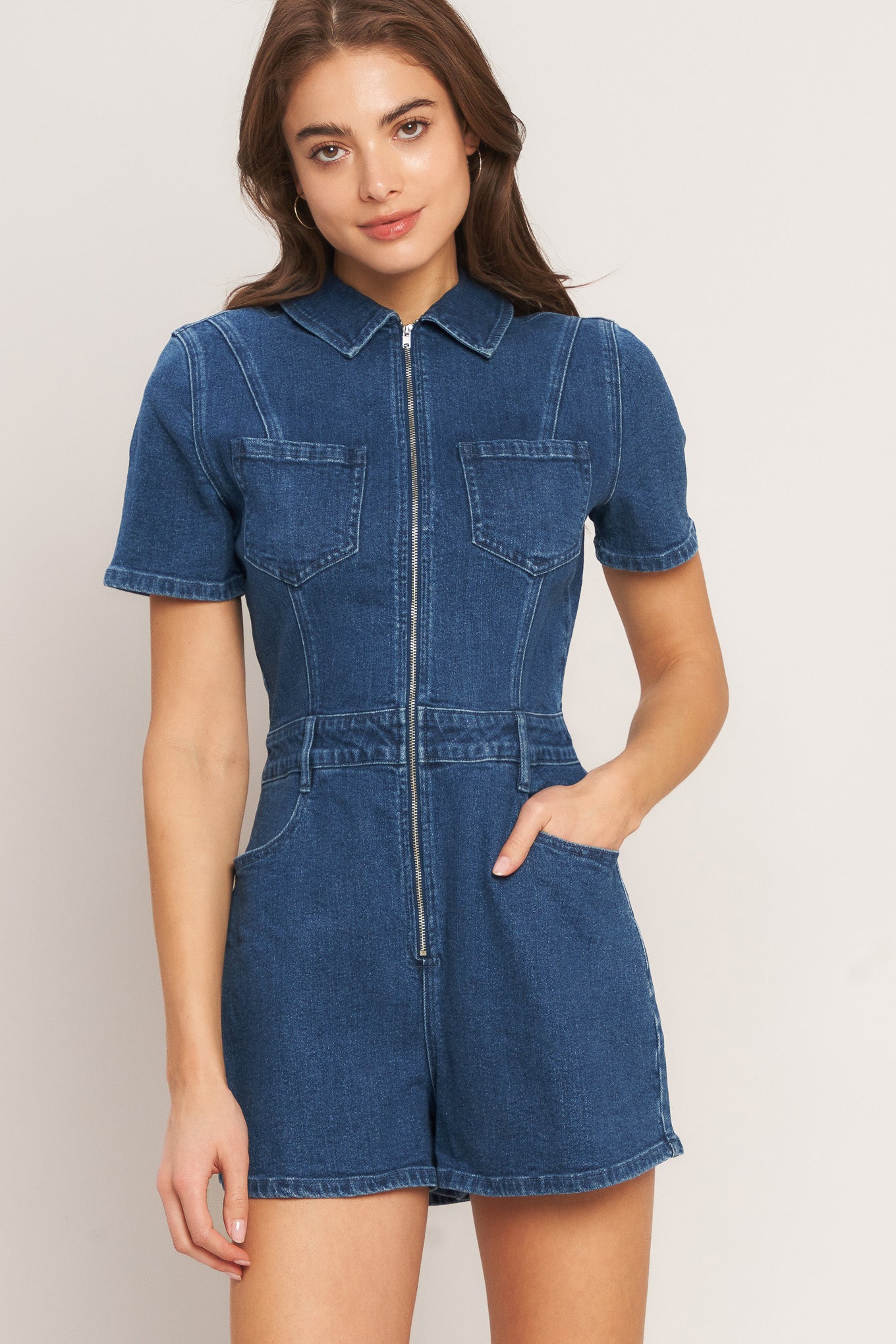 A washed denim romper featuring collar, front zipper closure, short sleeve and pockets