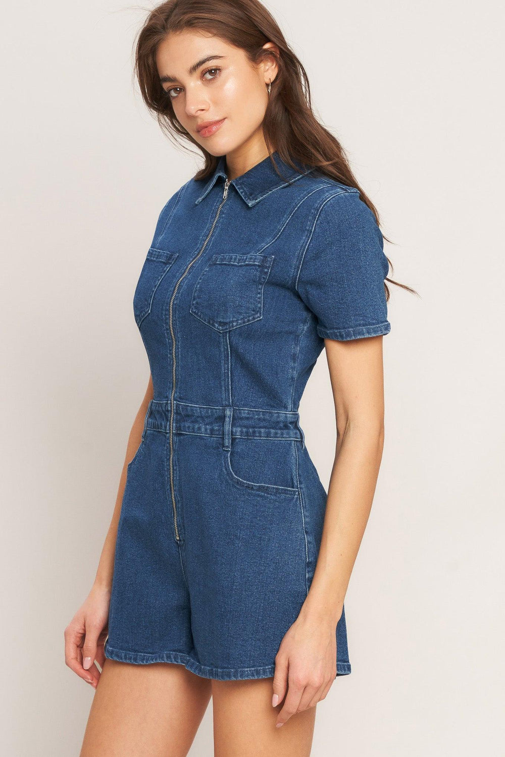 A washed denim romper featuring collar, front zipper closure, short sleeve and pockets