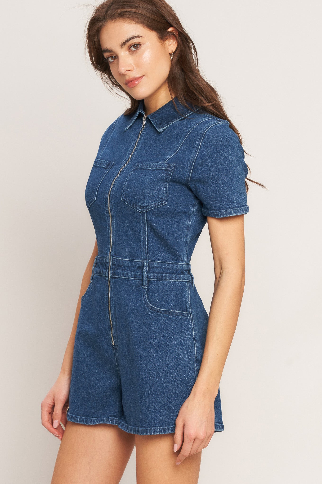 A washed denim romper featuring collar, front zipper closure, short sleeve and pockets
