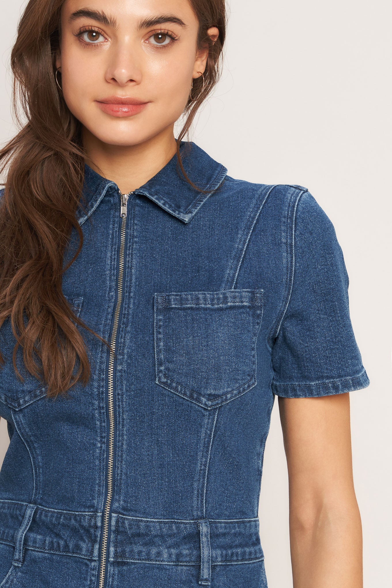 A washed denim romper featuring collar, front zipper closure, short sleeve and pockets