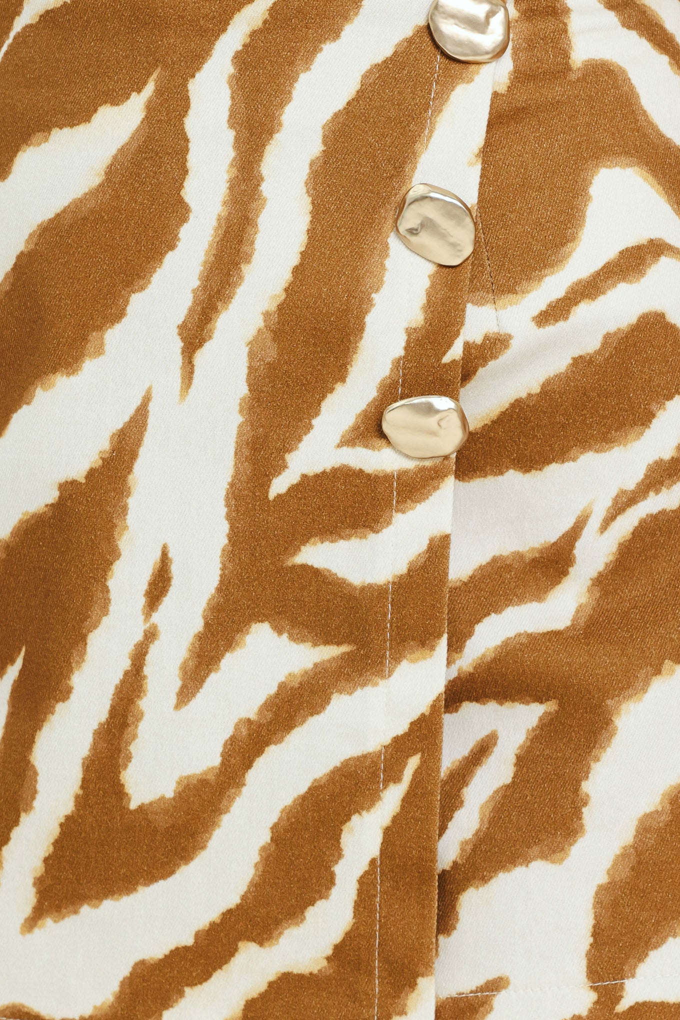 Close-up of a brown and white zebra-striped fabric with gold buttons | Flying Tomato