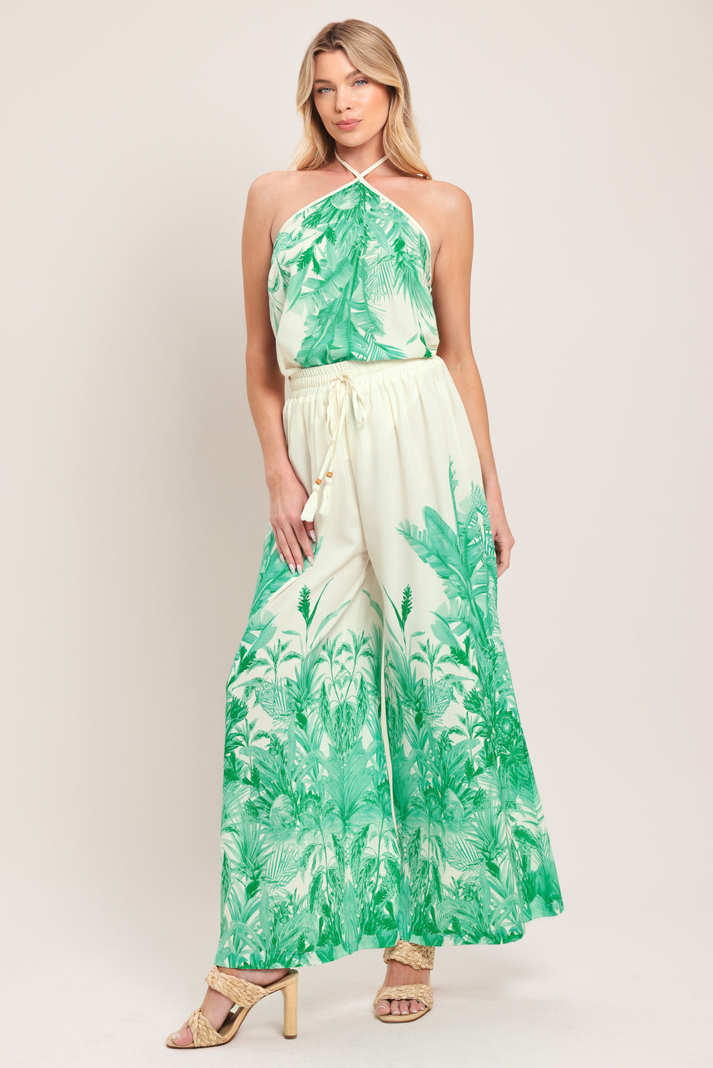 Woman wearing green and white tropical leaf patterned wide-leg pants with elastic waist and front tie | Flying Tomato