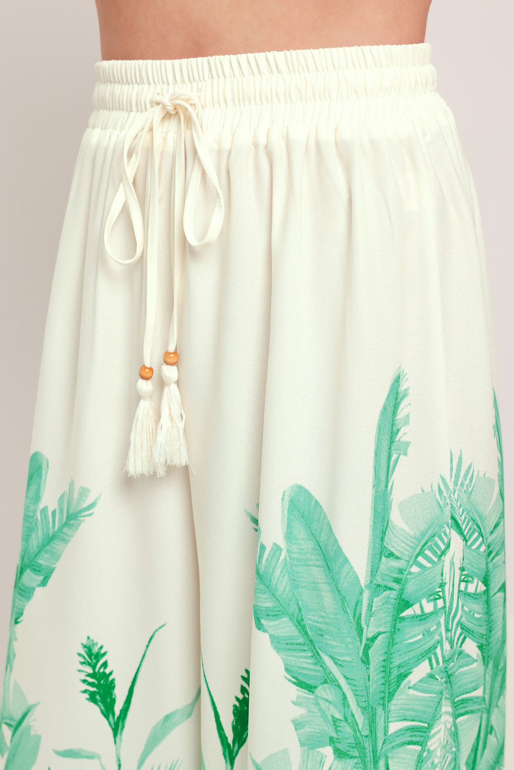 Woman wearing green and white tropical leaf patterned wide-leg pants with elastic waist and front tie | Flying Tomato