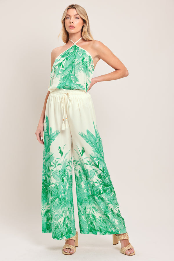 Woman wearing green and white tropical leaf patterned wide-leg pants with elastic waist and front tie | Flying Tomato