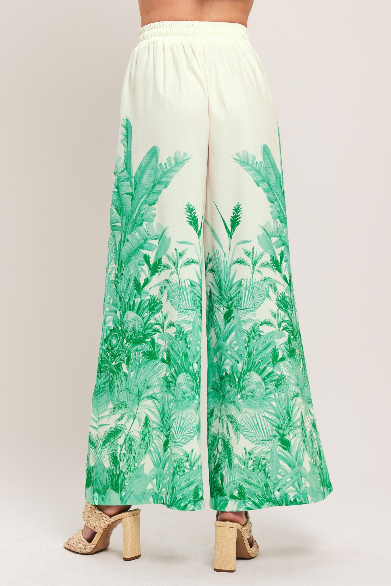 Woman wearing green and white tropical leaf patterned wide-leg pants with elastic waist and front tie | Flying Tomato