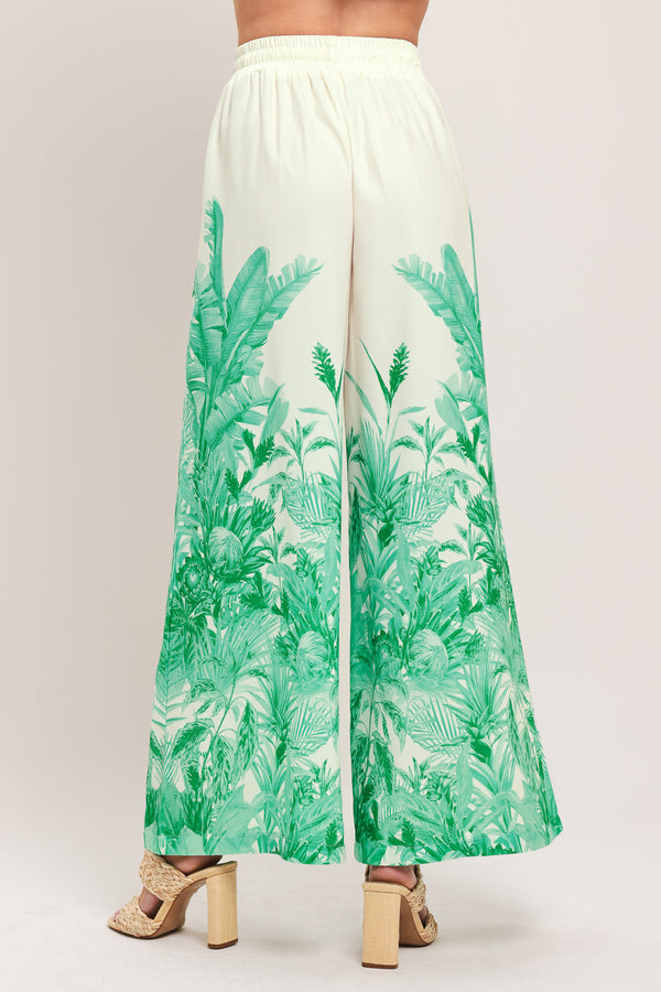 Woman wearing green and white tropical leaf patterned wide-leg pants with elastic waist and front tie | Flying Tomato